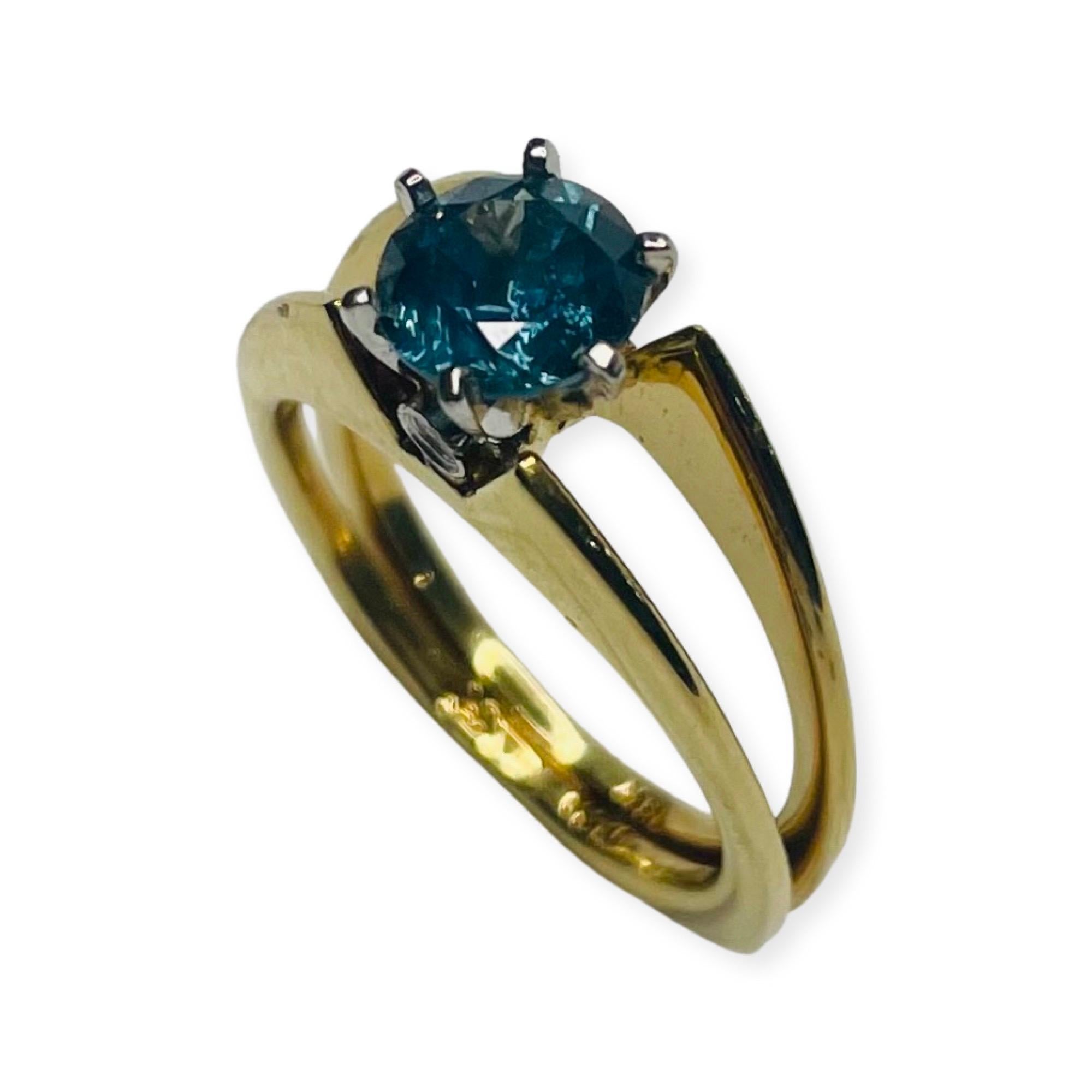 Lithos 18K Yellow Gold, Platinum, Montana Sapphire Ring.  The center stone is a 1.34 carat Montana Sapphire. This sapphire was mined in Philipsburg Montana. There are 2 full cut round brilliant diamonds bezel set one in the front and one in the back