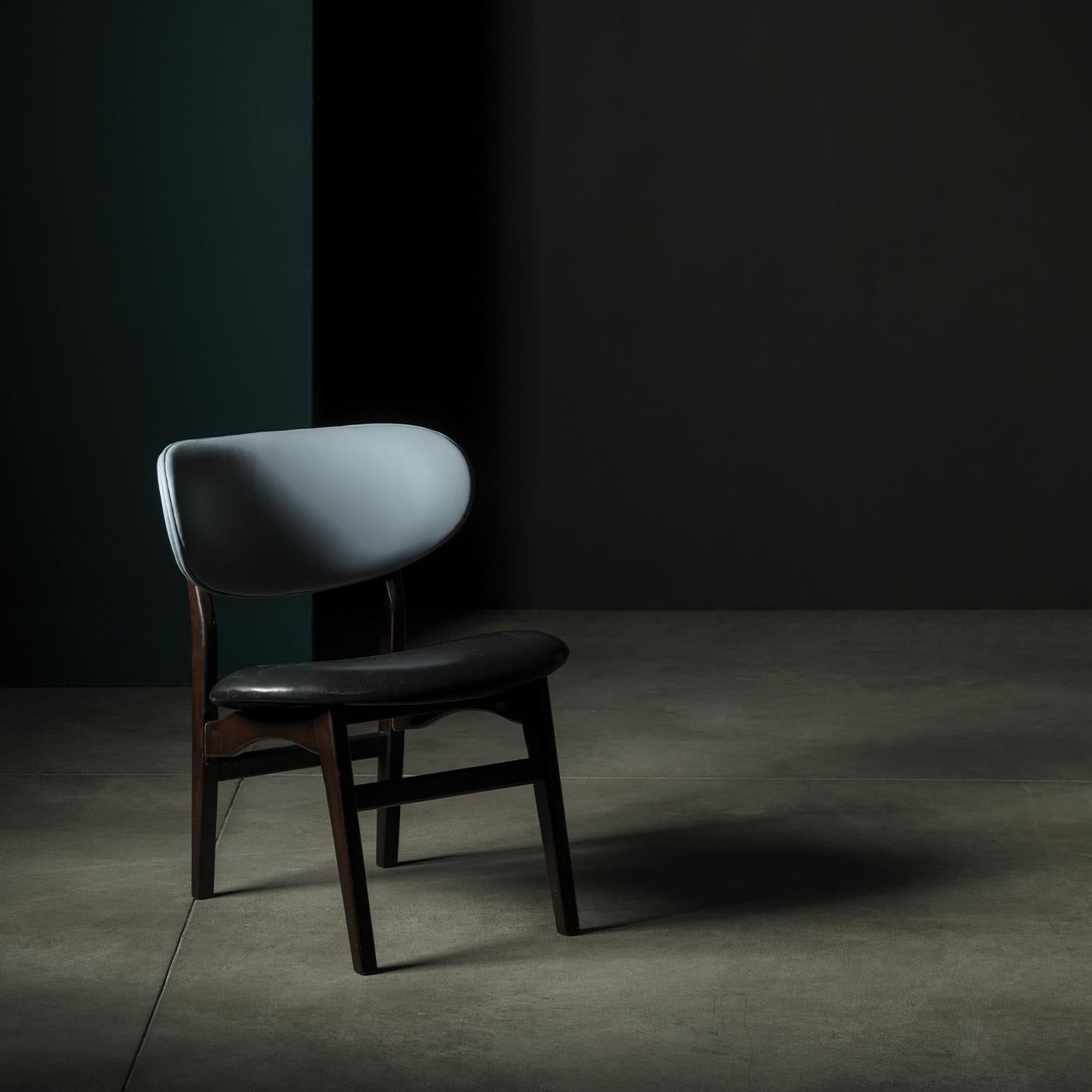 With a silhouette reminiscent of early 20th century design, this sleek, minimalist armchair features a wooden structure with a dark walnut finish. A black leather seat stands in contrast to its back in light blue leather, which adds a touch of