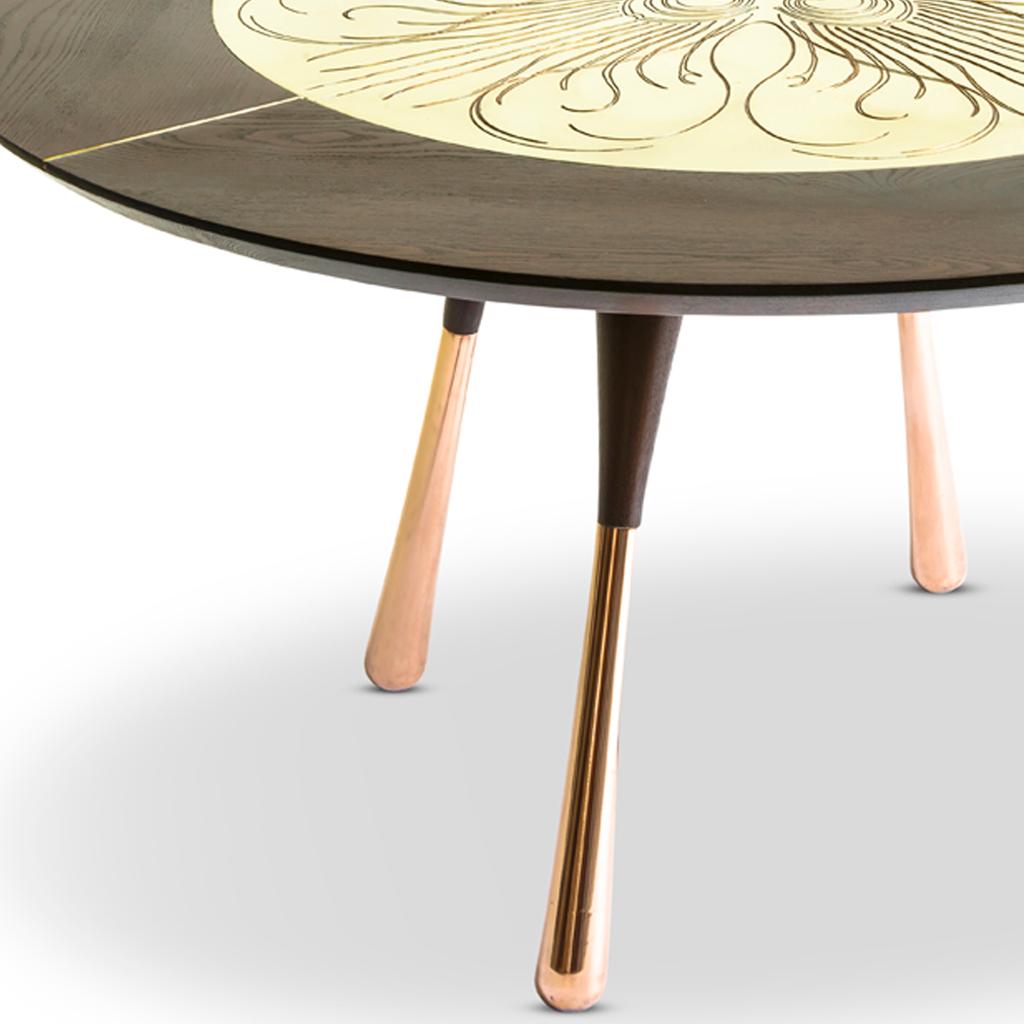 La mesa de comedor redonda Little Miss Fat tiene la base y el tablero de madera de roble teñido. La tapa de madera tiene una incrustación de latón macizo con un grabado de plumas de pavo real. Las patas son de madera con el fondo chapado en