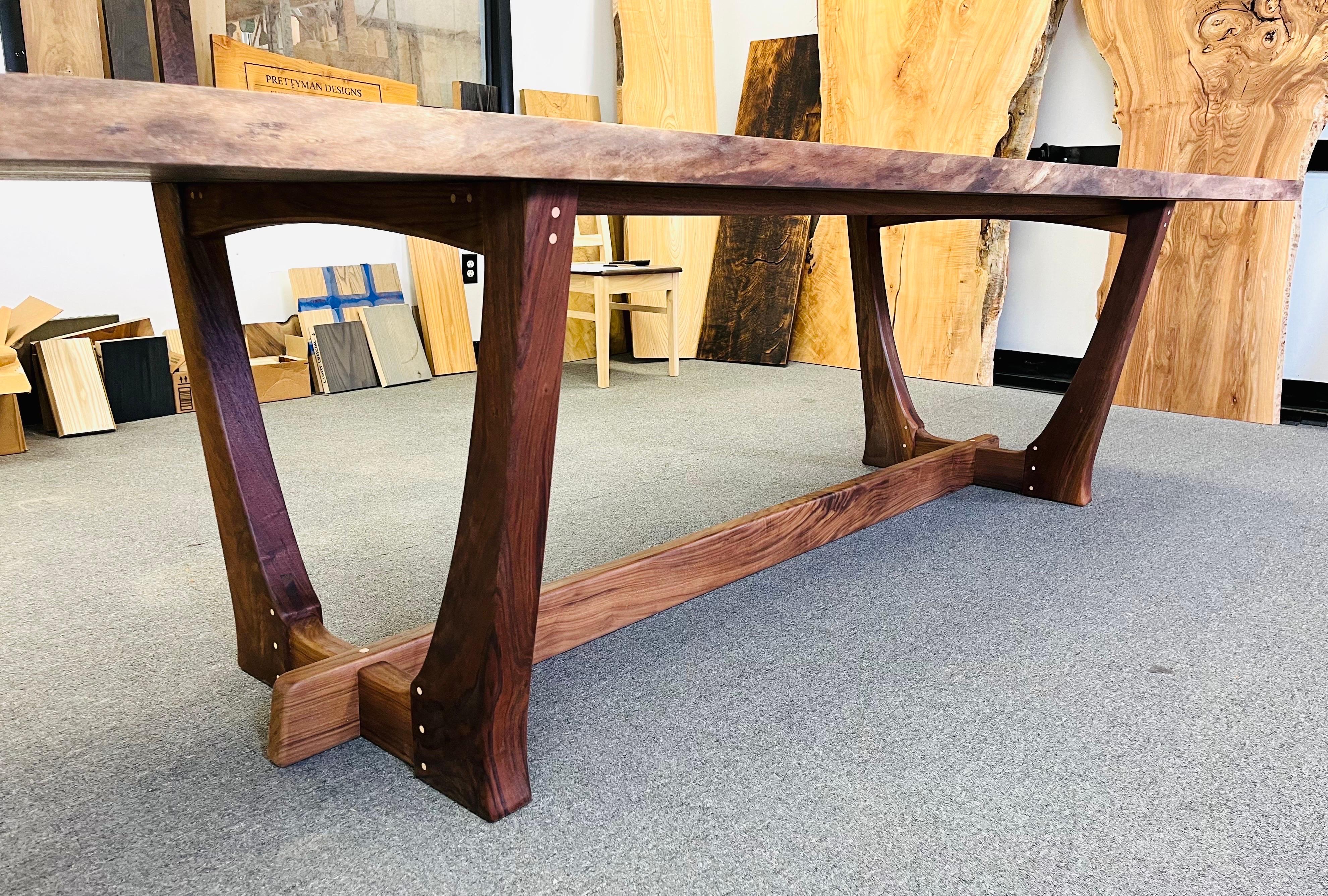 A beautiful custom live edge dining or conference table constructed in a sculptural Black walnut frame underneath of a monumental English walnut freeform tree slab in the manner of George Nakashima with tones that also nod to Phillip Lloyd Powell. A
