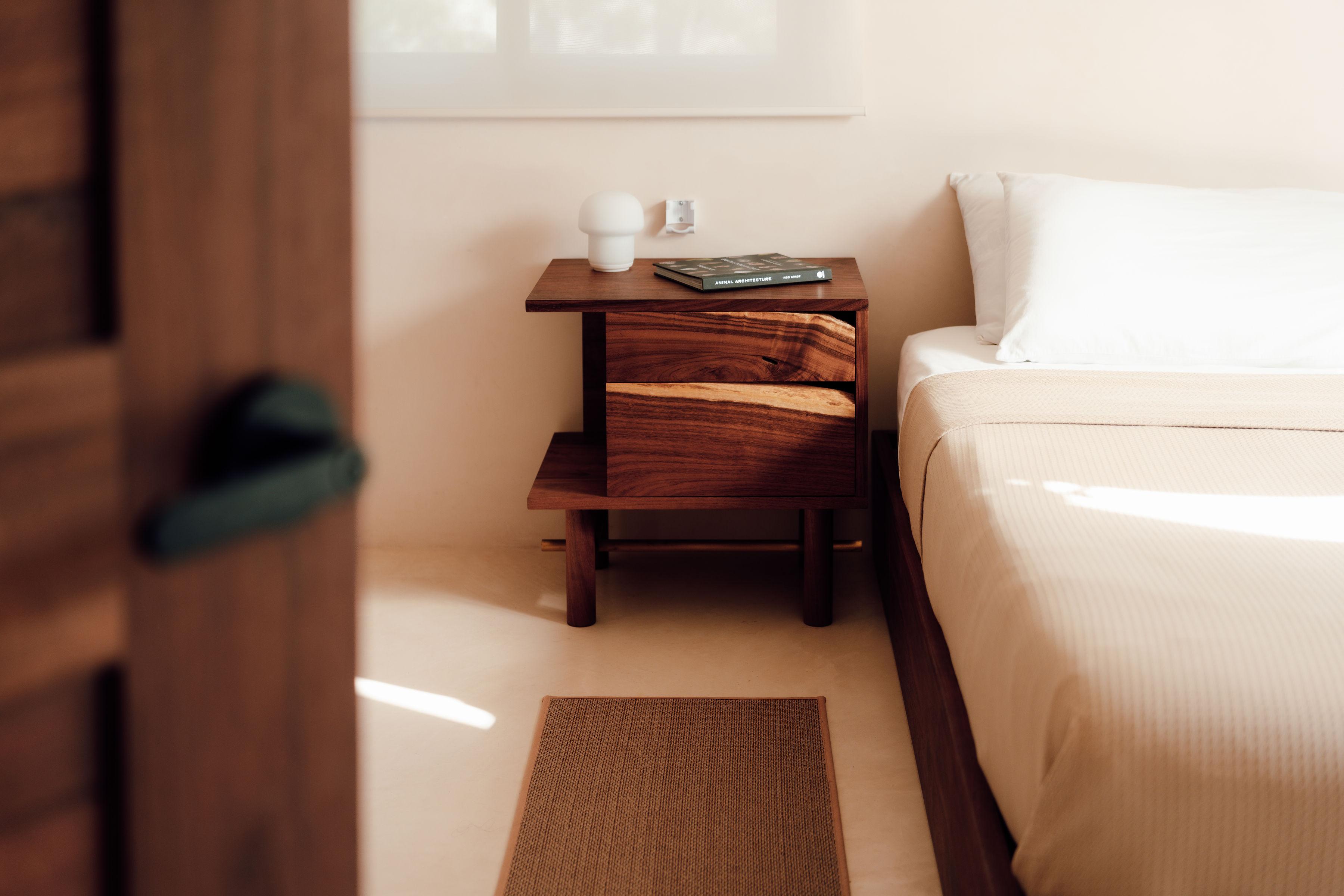 Le design de la table de nuit Ocum est caractérisé par la recherche de proportions équilibrées, la simplicité des formes de base et une construction minimaliste. Les textures contrastées du noyer des Caraïbes et les détails en bronze lui donnent