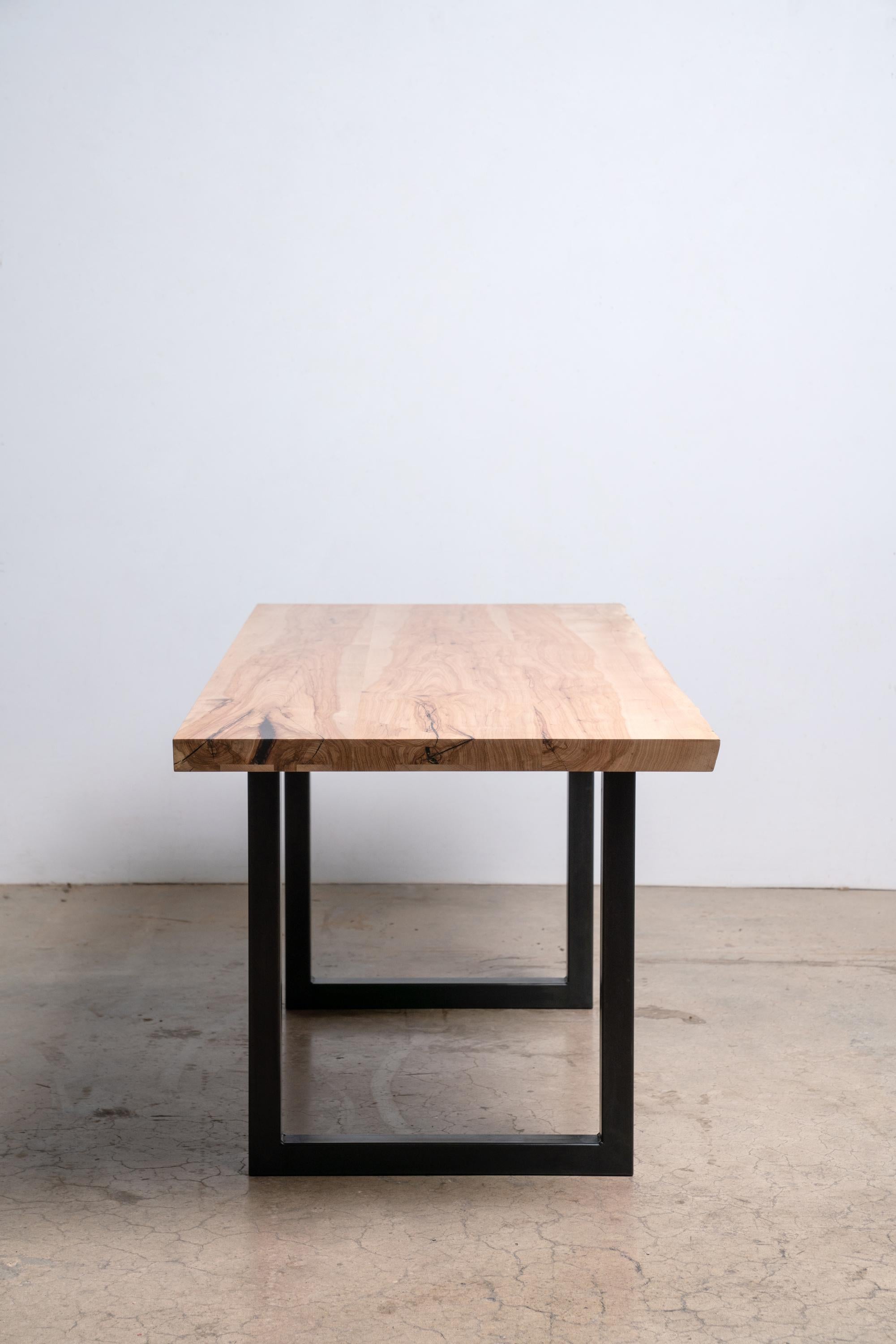 Wir nennen unseren Pekannuss-Tisch mit klarer Kante auf einem modernen, schwarzen, quadratischen Stahlgestell einen 