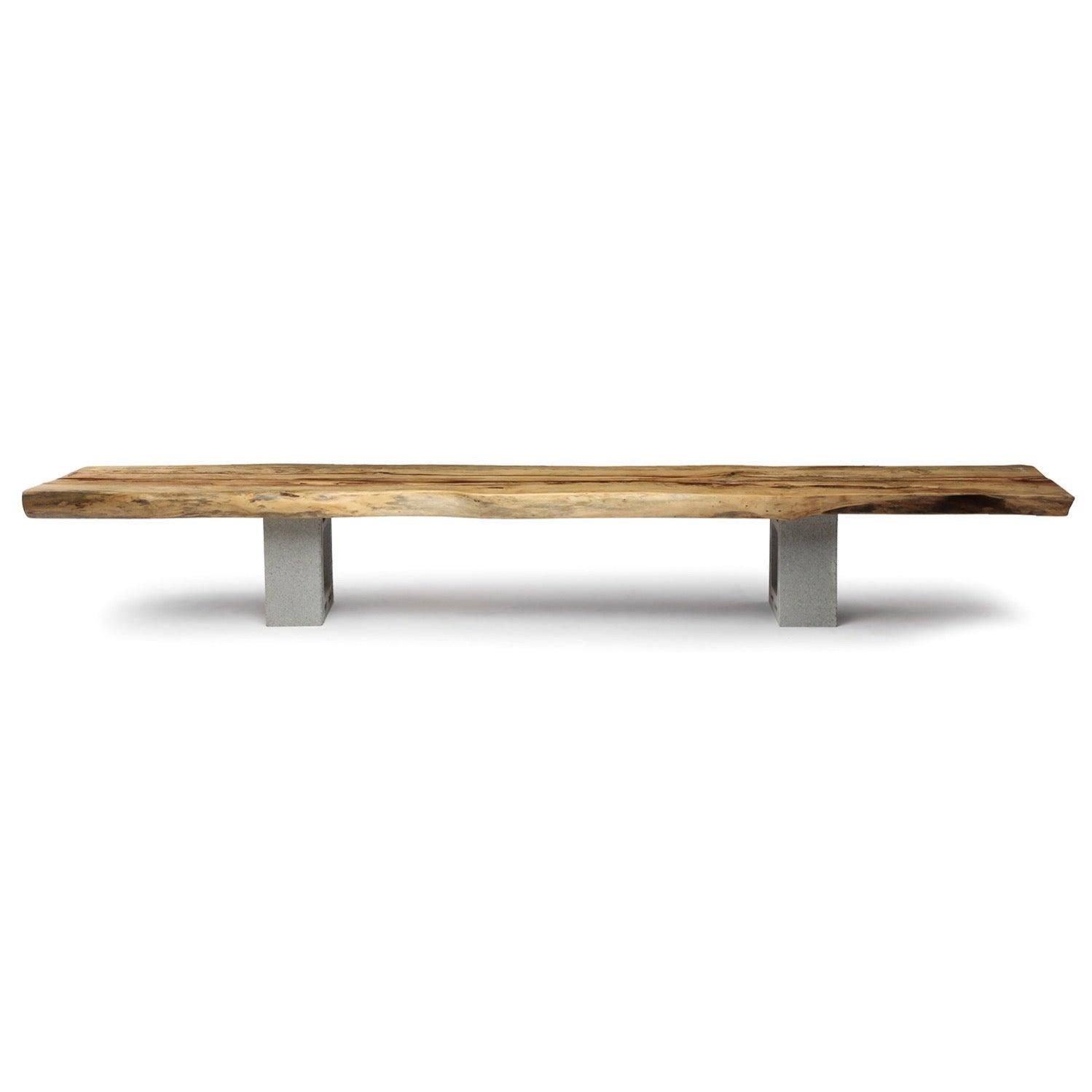 Une table basse ou un banc en planches massives taillées à vif reposant sur une base de parpaings fabriqués par l'artiste.