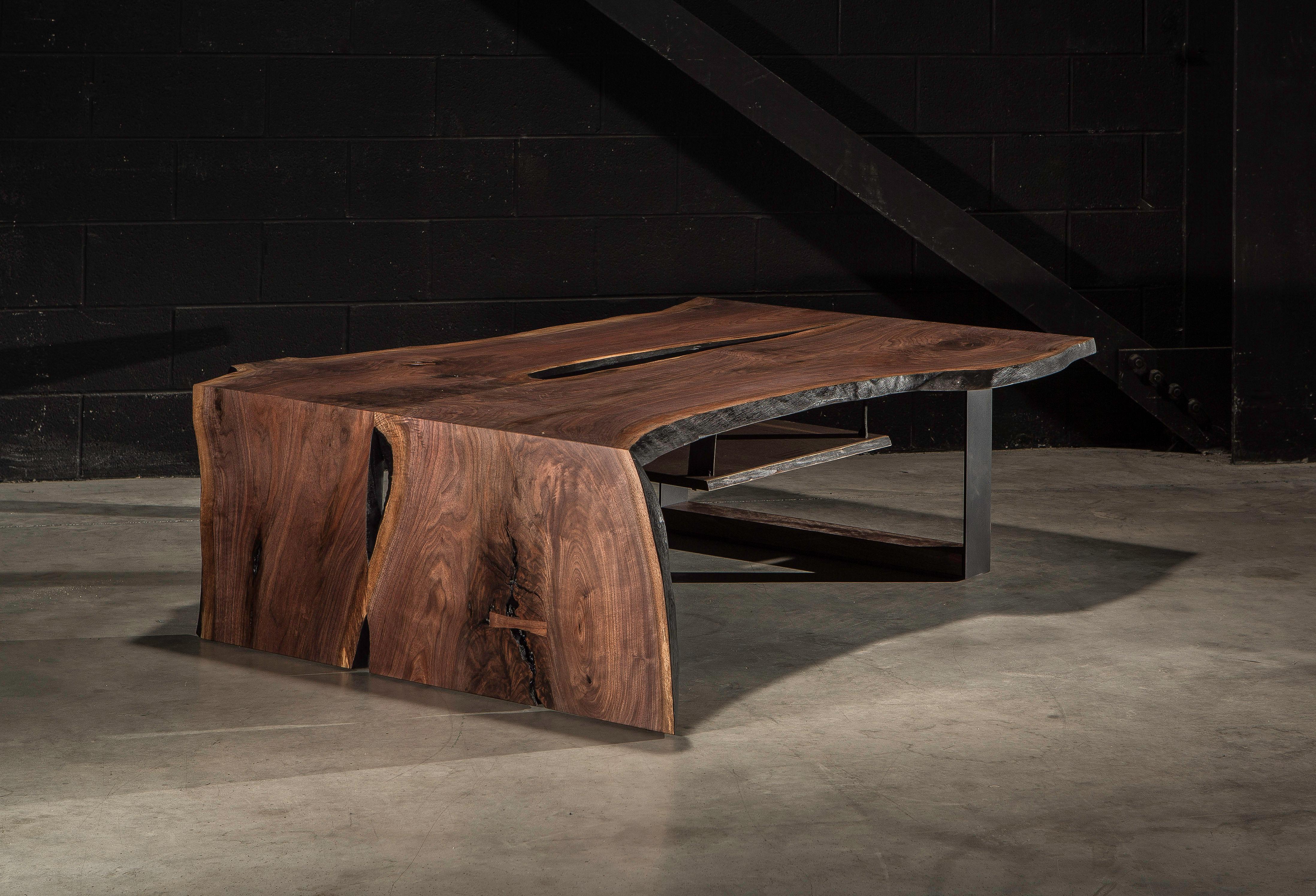 Two sister slabs of figured walnut create an asymmetrical waterfall coffee table with an organic live edge. 

Contrasted with a solid blackened steel base. 

Undermount walnut shelf, suspended by leather straps.

The pictured table is a prototype -