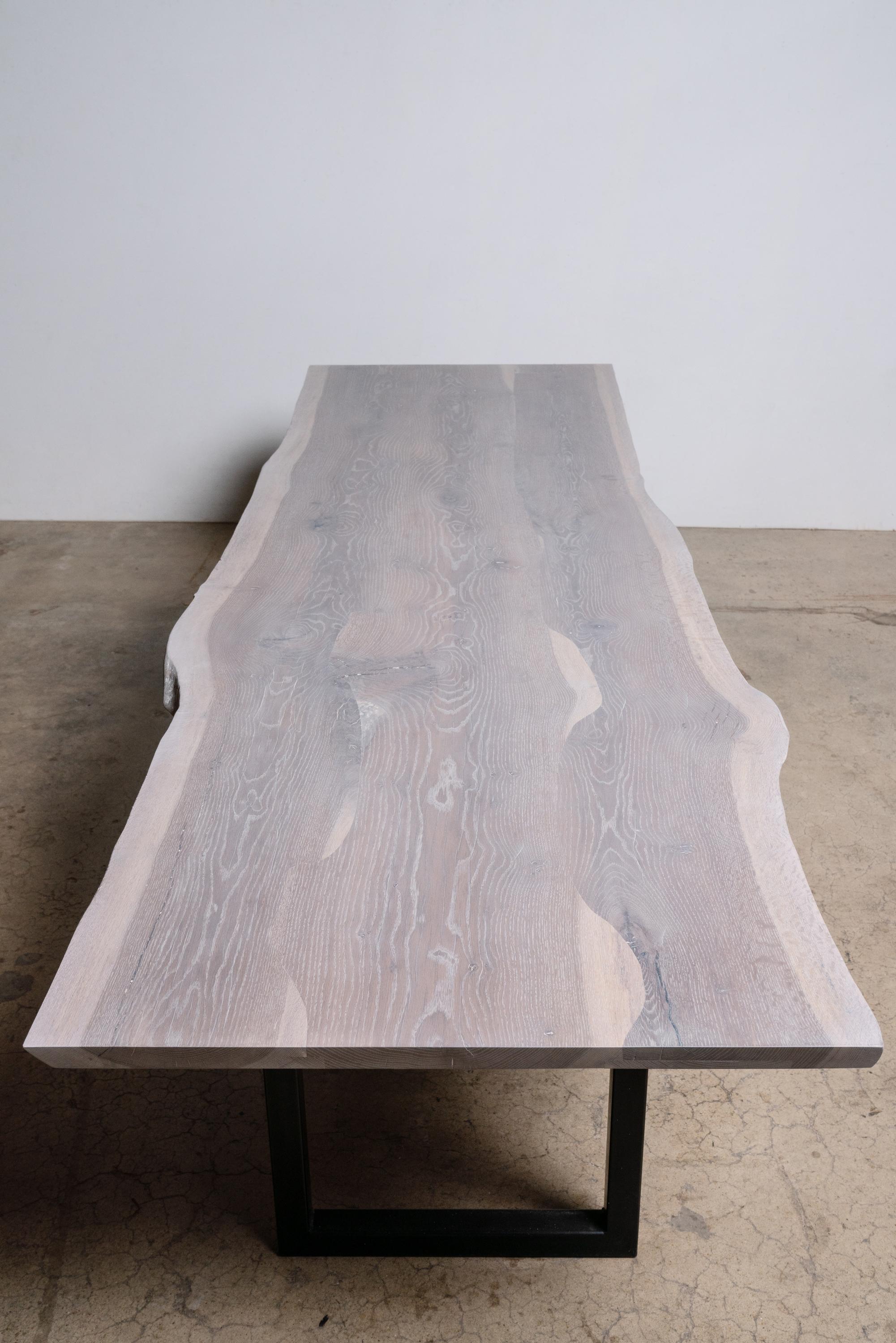 Nous appelons notre table à bord vif en chêne blanc finition grise sur base carrée en acier noir moderne une 