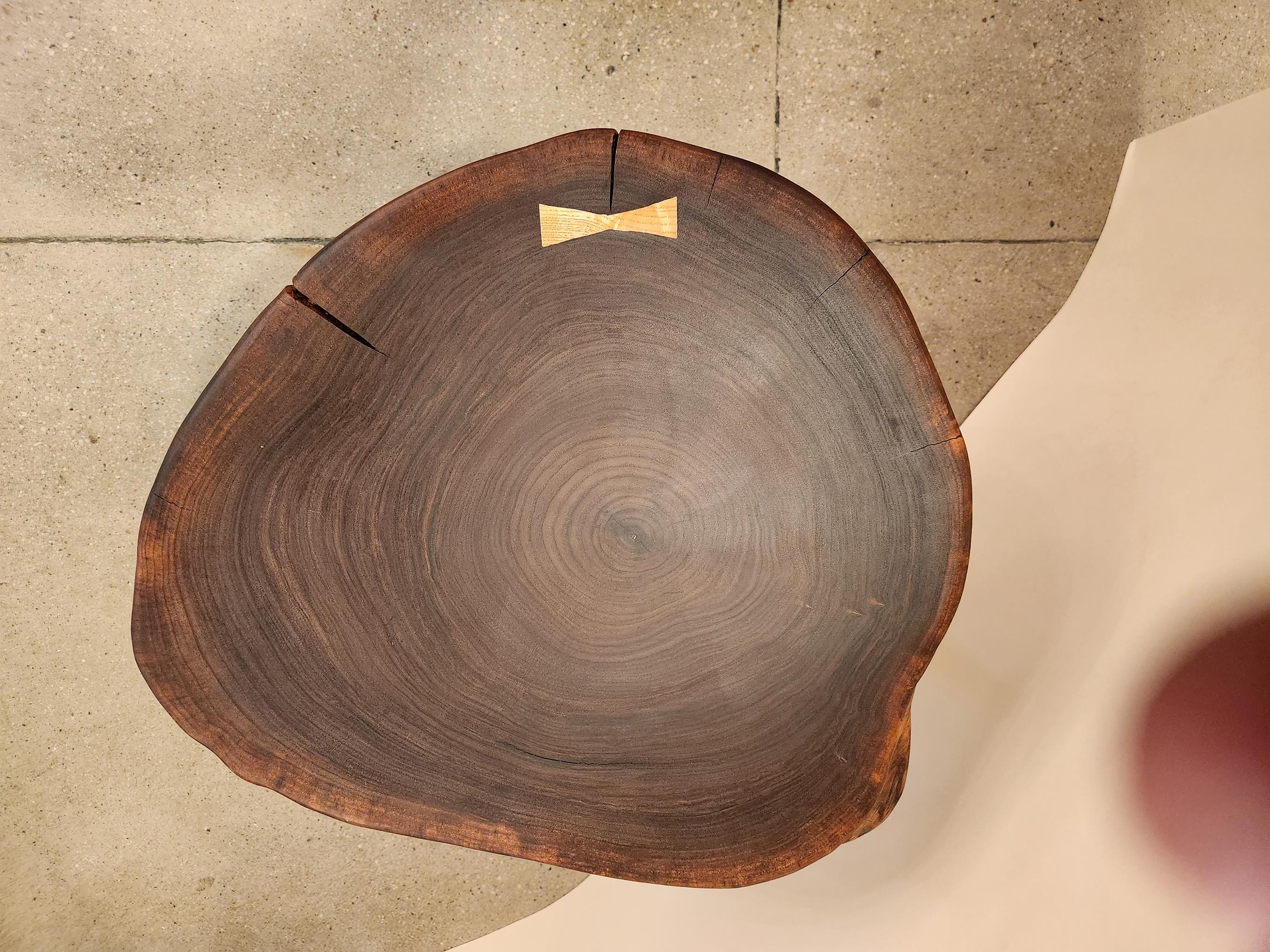 This cookie slab coffee table with a bow tie key is a perfect piece that is both functional and artisanal. It is made from walnut wood which is known for its strength, grain and color. The wood was polished to a smooth finish and coated with several
