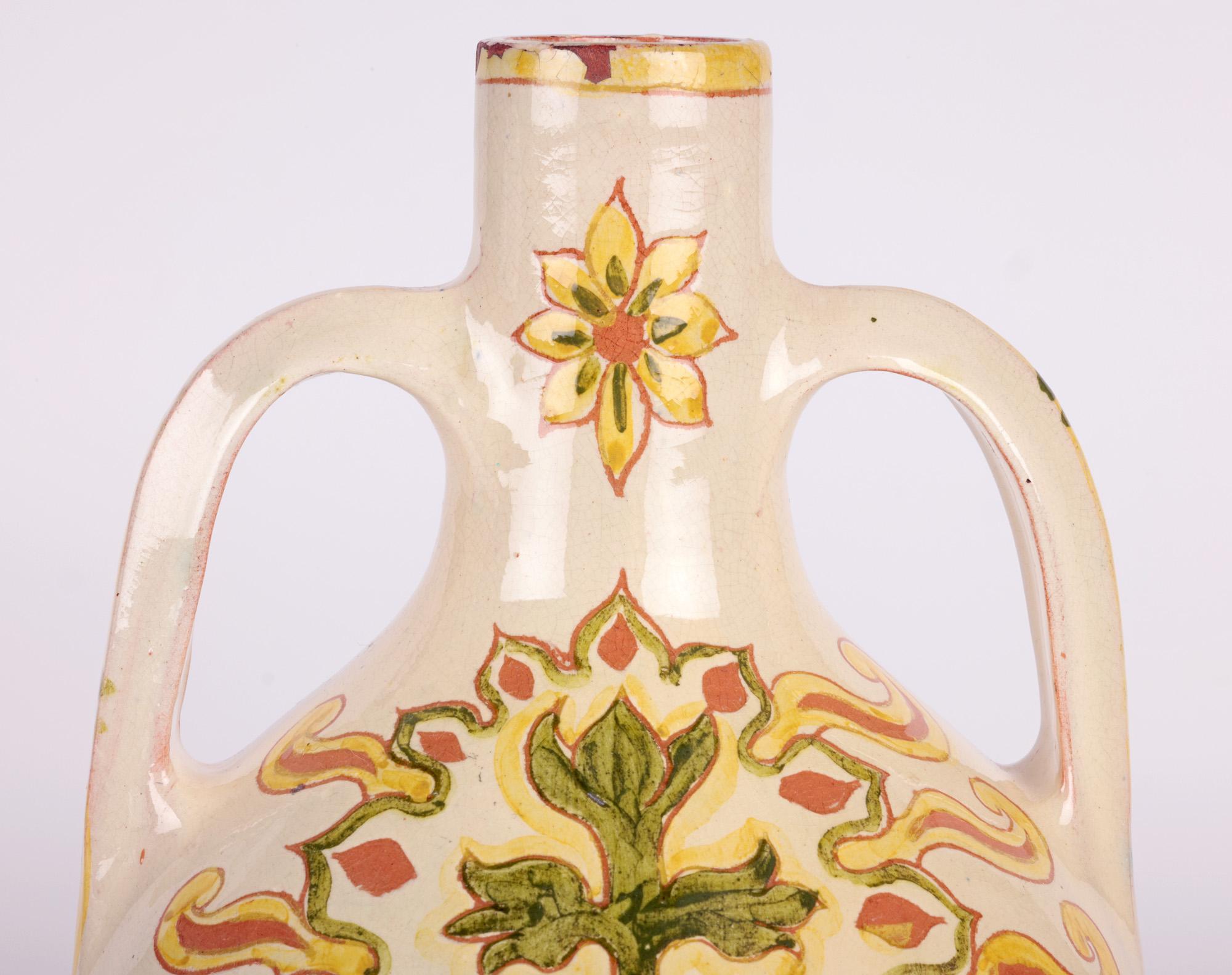 Eine stilvolle und gesuchte englische Arts & Crafts Vase mit zwei Griffen, handbemalt von Lizzie Wilkins für Della Robbia Birkenhead und datiert 1896. Die Vase in Fahnenform ist aus Terrakotta-Ton gefertigt und steht auf einem schmalen runden Fuß.