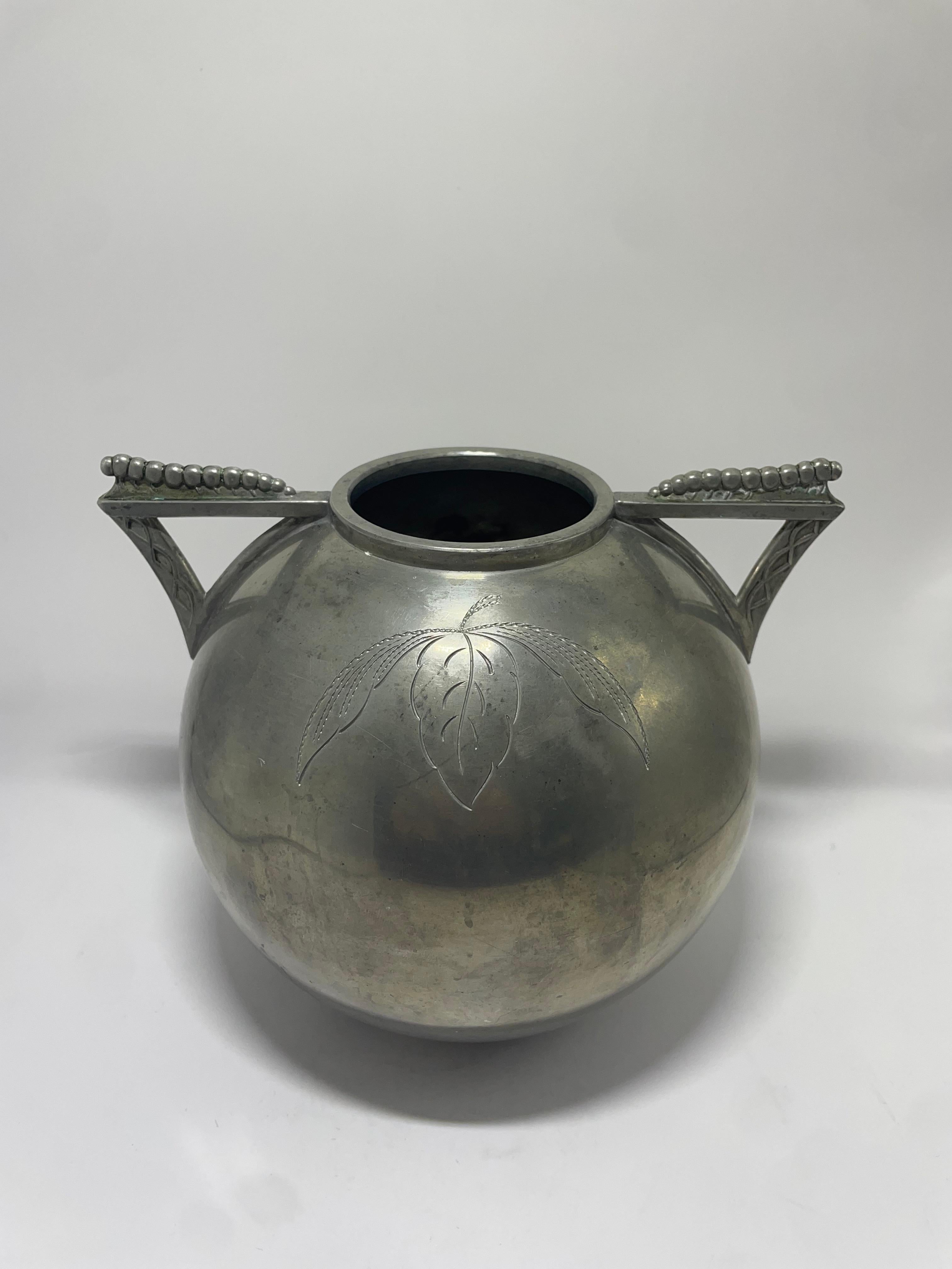 Elegant and rare Swedish pewter vase designed by Lundin & Lundberg (L&L), dating to 1935. This rounded vessel features delicately engraved foliage motifs on the front, highlighted by striking triangular handles with beaded detailing. Crafted in a