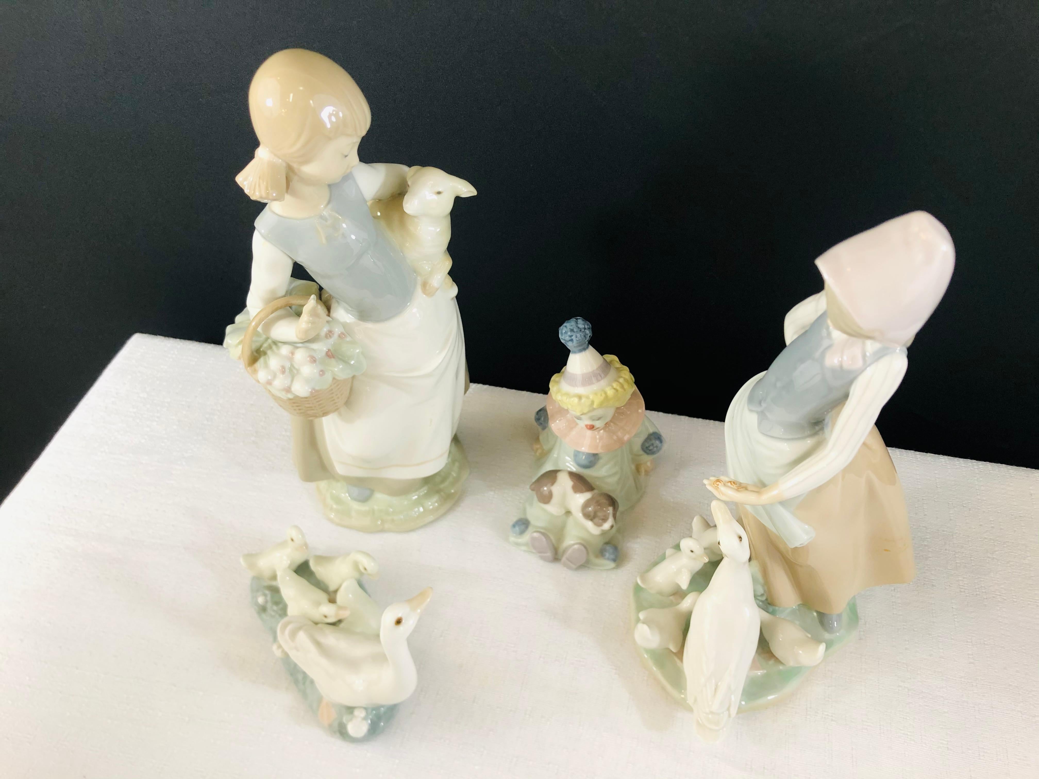 A set of 4 Lladro (Spain) porcelain figurines. One figurine of a woman feeding ducks, one figurine of a woman holding a lamb, one of a group of ducks and the last one is a clown. Each figurine is signed in the bottom.
Figurine 1: 5” L x 3.75” H x 2”