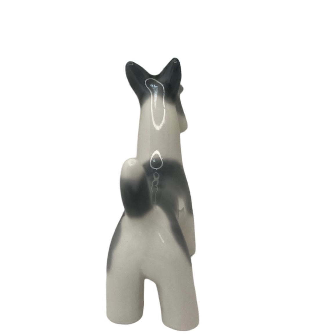 This is a Lladro porcelain mini figurine of a dog. It depicts a hand painted grey blue and white Scottish Terrier dog standing up and frowning. The Lladro Nao hallmark is below the figurine.