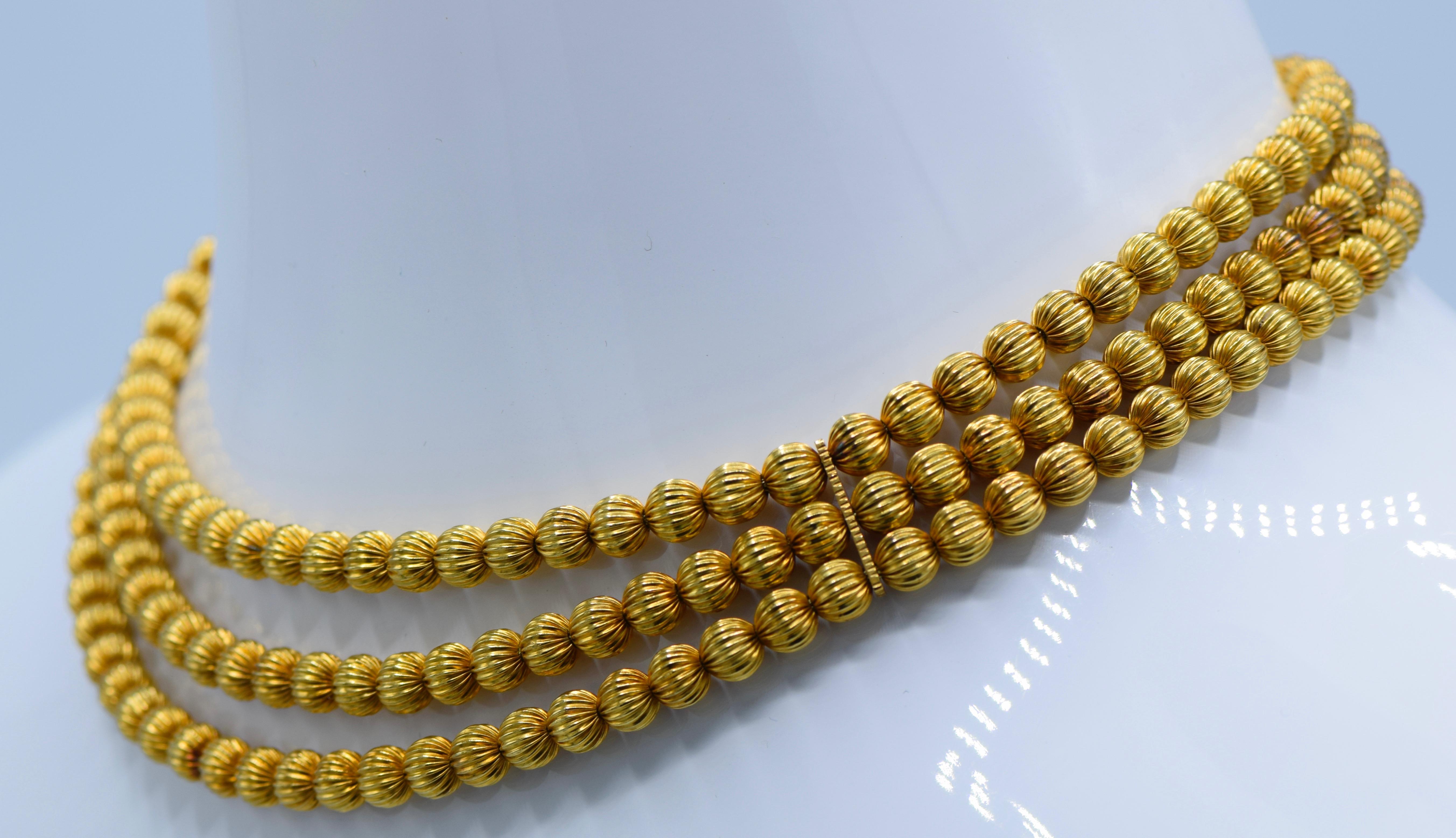 18 kt., composed of three strands of finely ribbed gold beads, signed Ilias Lalaounis, Greece, with maker's mark, 
approximately 64 dwts. 

Length 16 3/4 inches. 

Rich yellow gold color. Some of beads of section near female end of clasp of lighter