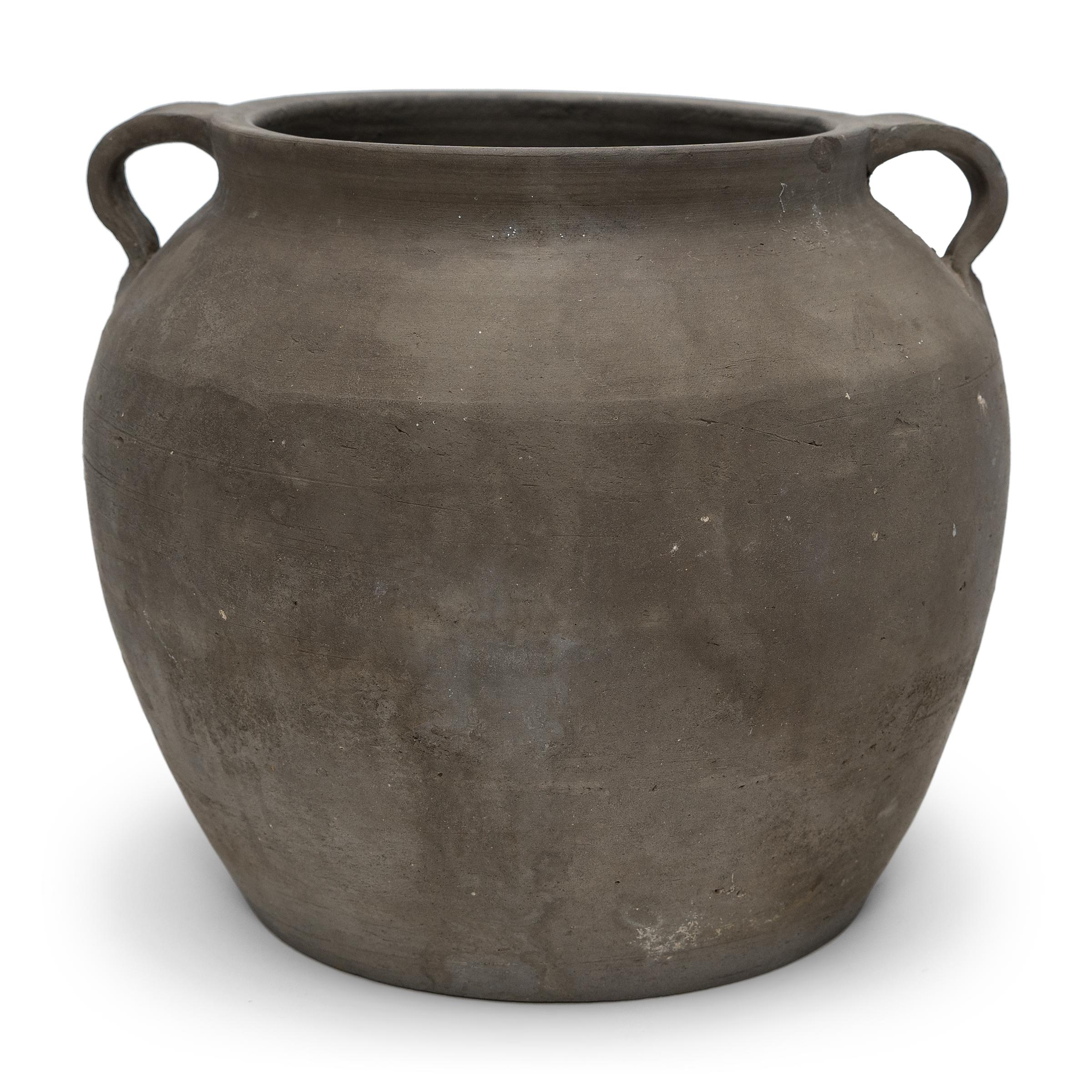 Charged with the humble task of storing dry goods, this small earthenware jar was hand-shaped in the early 20th century with balanced proportions and a beautifully irregular unglazed surface. The round jar has a tapered form with a narrow base, high