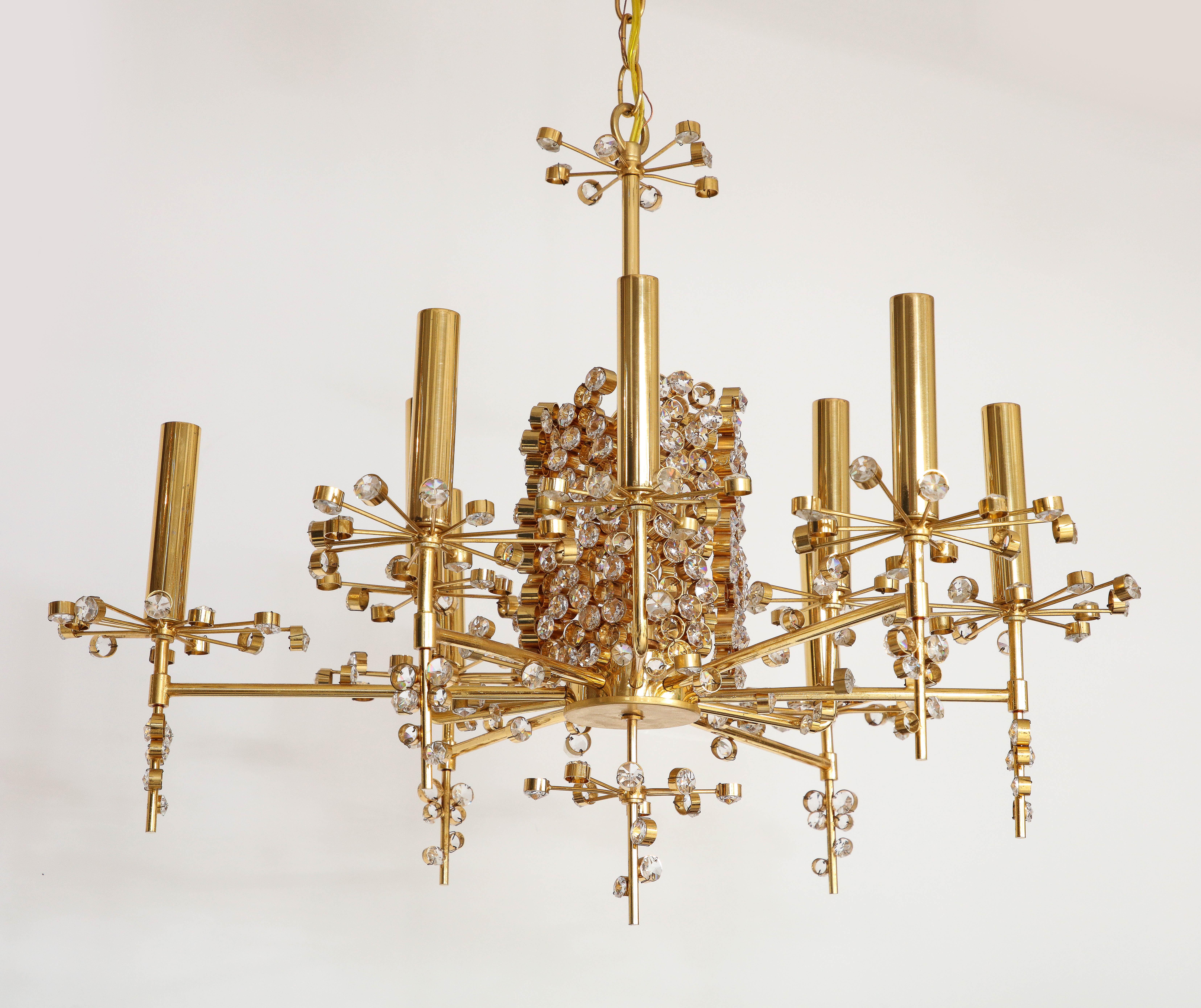 A J. & L. Lobmeyr nine light chandelier designed by Hans Harald Rath with a central cylindrical body encrusted with faceted crystals each encased in brass from which nine arms orbit the center adorned with individual spokes of brass and