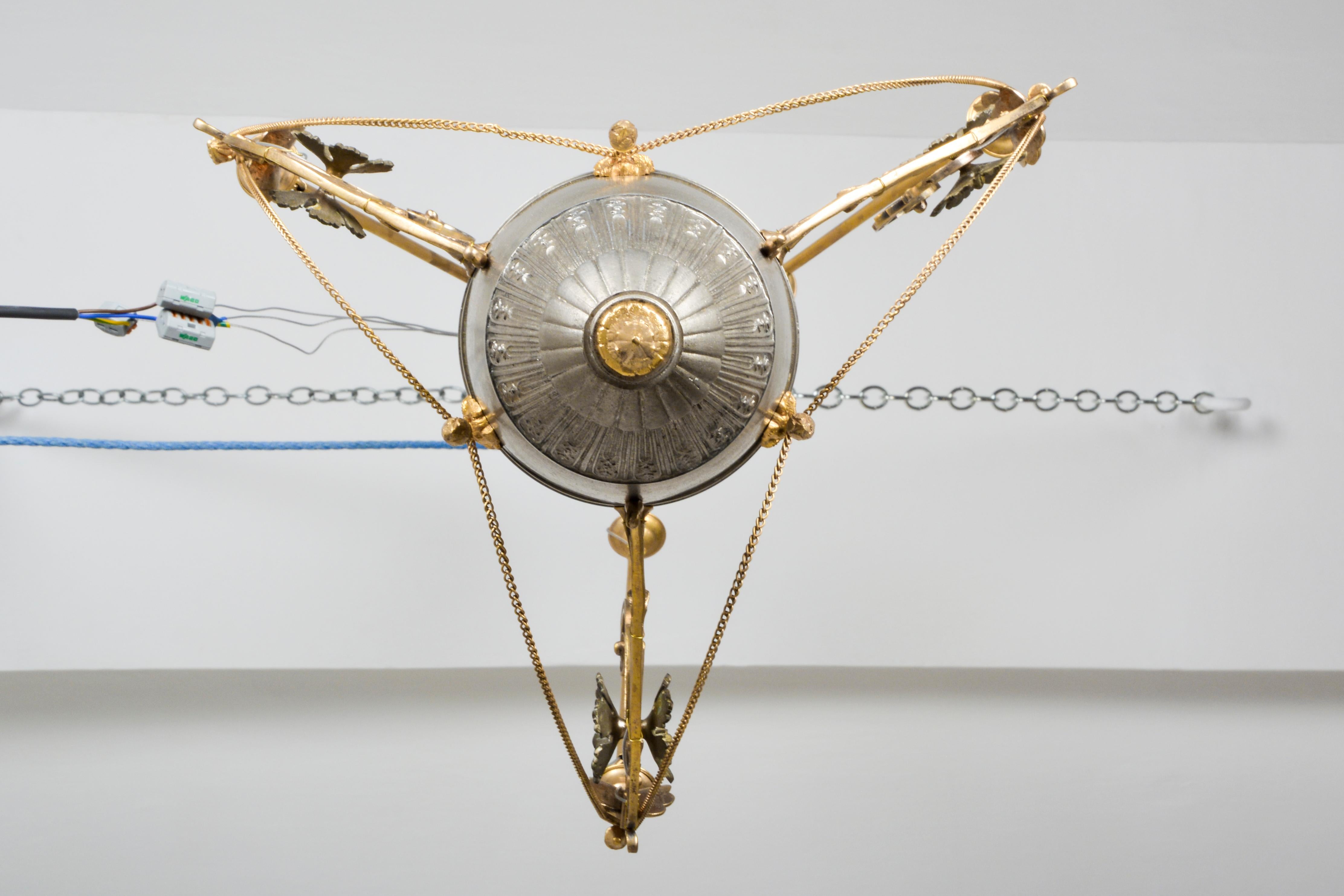 This is a magnificent eternal light pendant from the late 19th century. It has a wonderful finish of contrasting gold and tin. The brass parts are elaborately cast and refined in the style of Theophil Hansen. The central glass flame is a replacement