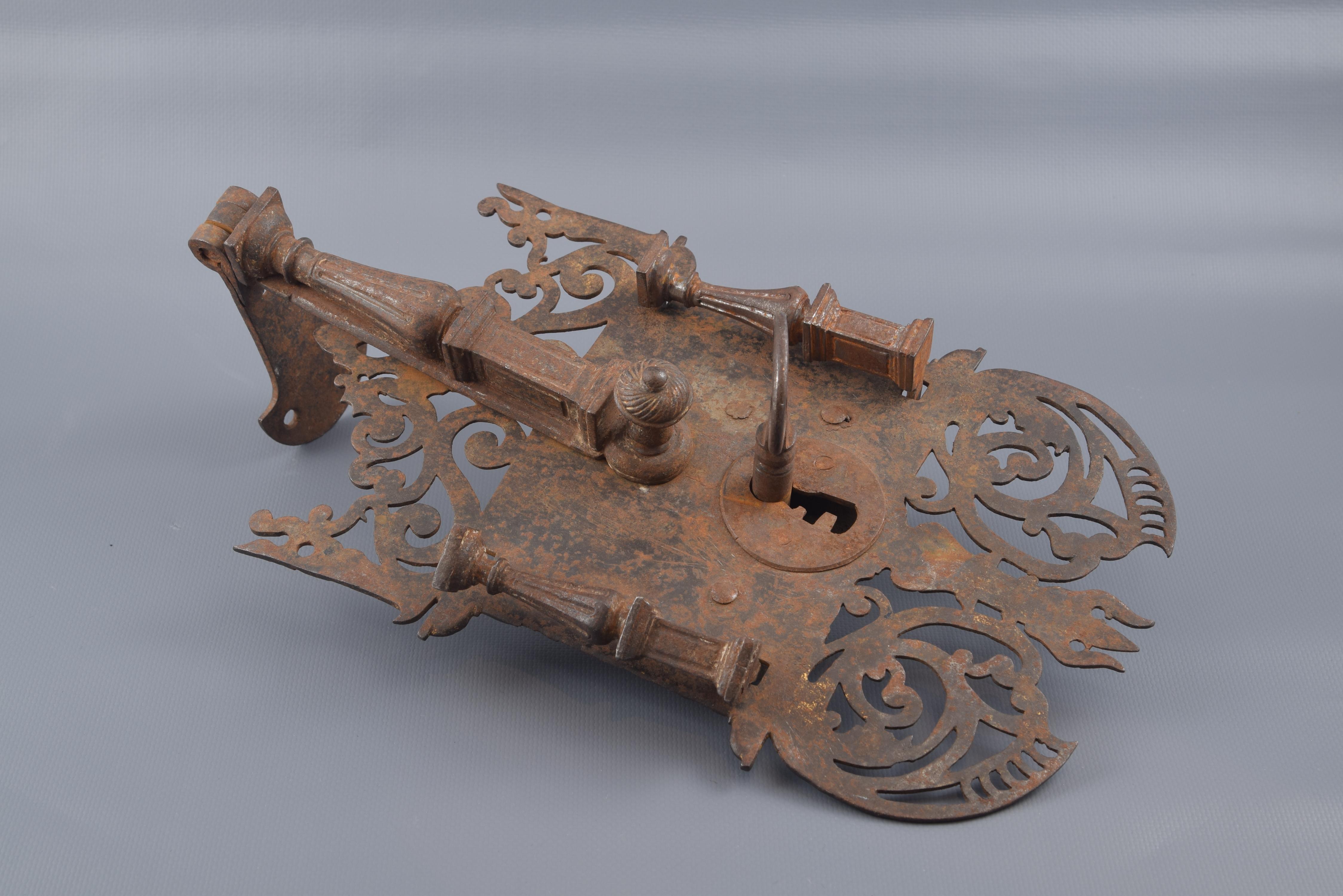 Wrought iron lock, composed of the upper part that is fixed to the furniture, the area of the bolt and an openwork decoration (based on simple plant elements, scrolls and architectural details) with classicist architectural elements (columns on