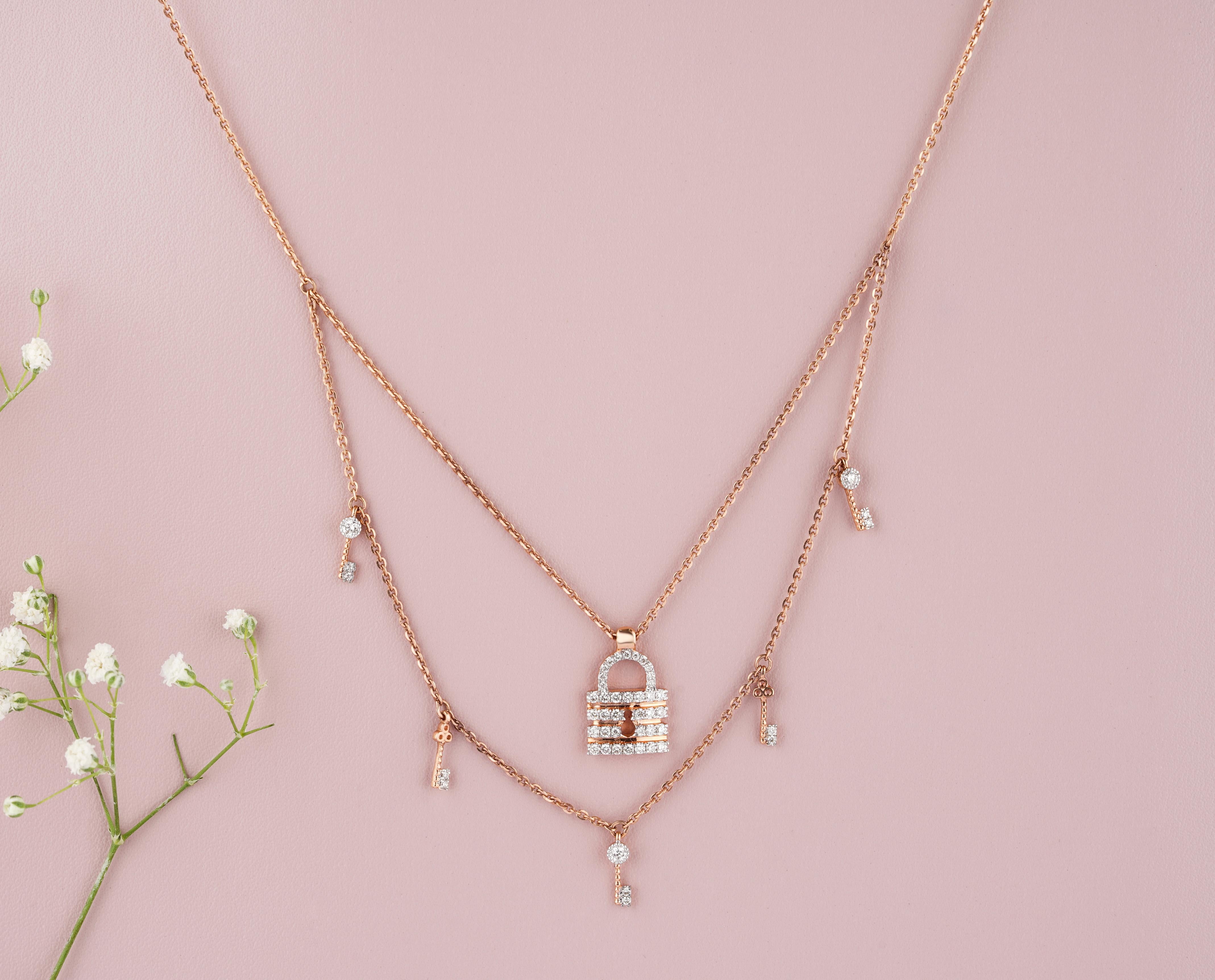 The Lock & Key Diamond Charms Necklace is a stunning piece of jewelry made from 18k solid gold. It features a double-layered design, with one layer showcasing a lock charm and another featuring key charms. The lock pendant is adorned with exquisite