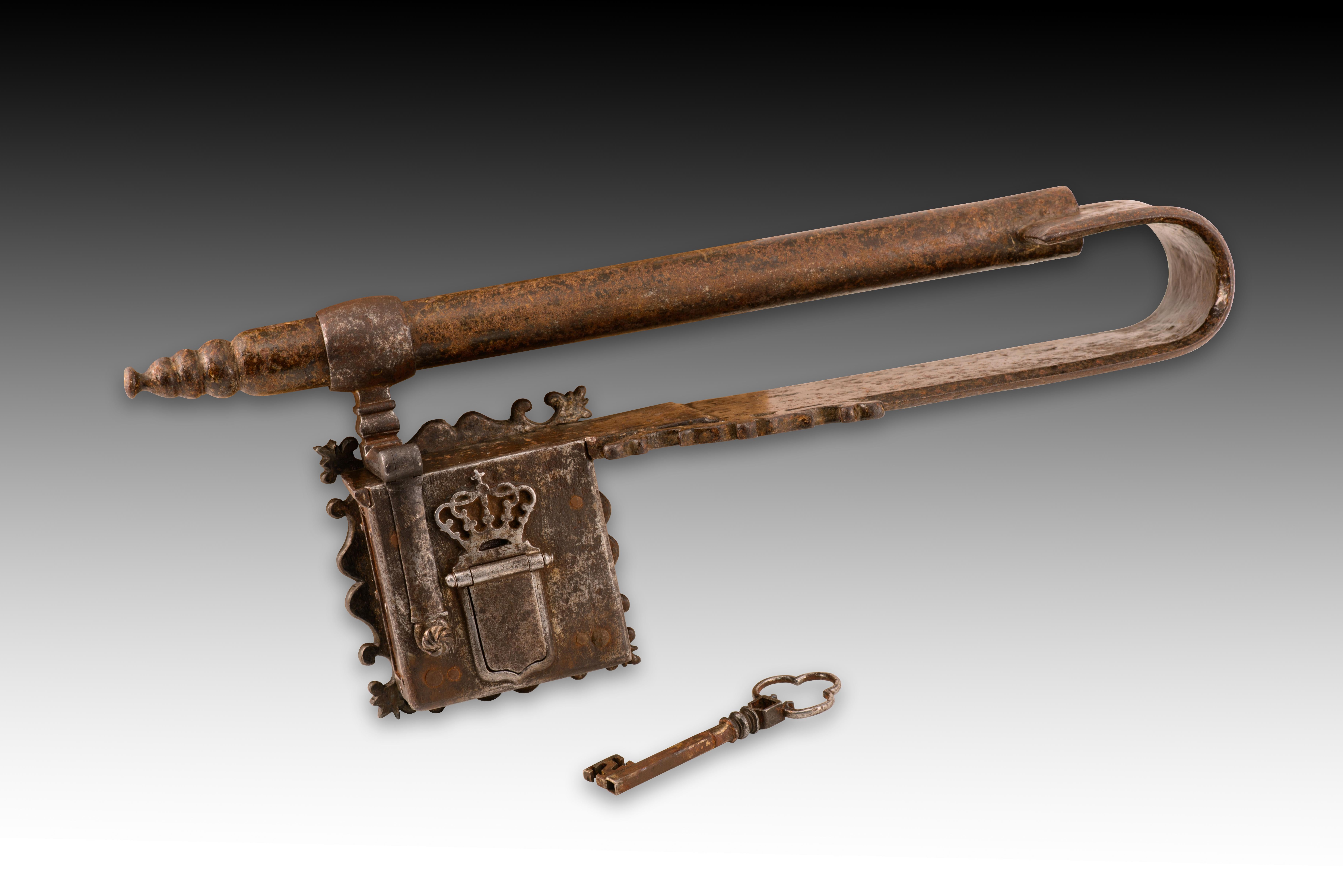 Cerradura. Hierro forjado. Spanish School, siglo XVII. 
El cerrojo de hierro forjado con llave tiene un mecanismo de pulsador en la parte inferior derecha para levantar la tapa que oculta el ojo de la cerradura. Se abre en dos pasos introduciendo la