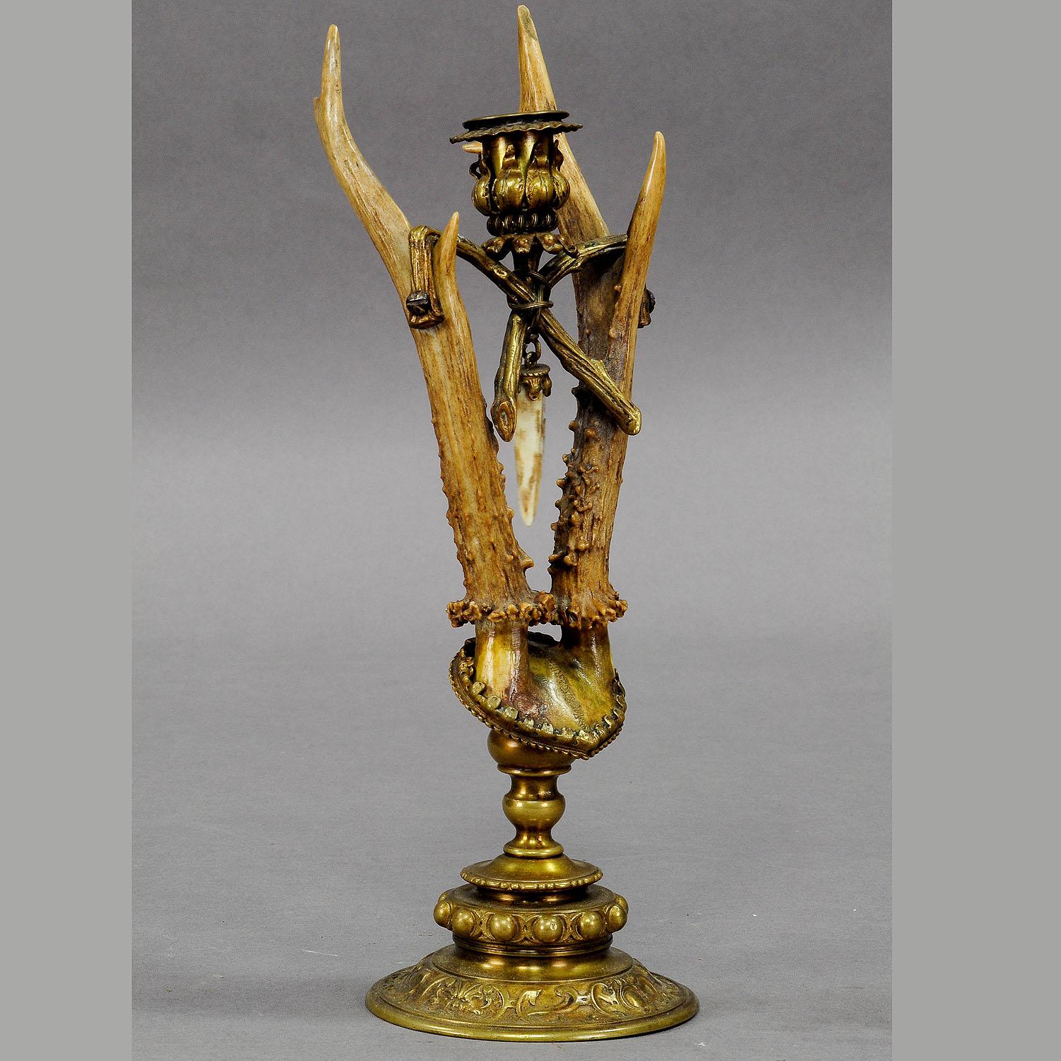 A decorative candleholder which is made of deer antlers mounted on a brass base. A roe deer trophy at the center, cased with brass. It is decorated with a wild boar tooth pendant. The candleholder is executed in Germany ca. 1880.

At the beginning