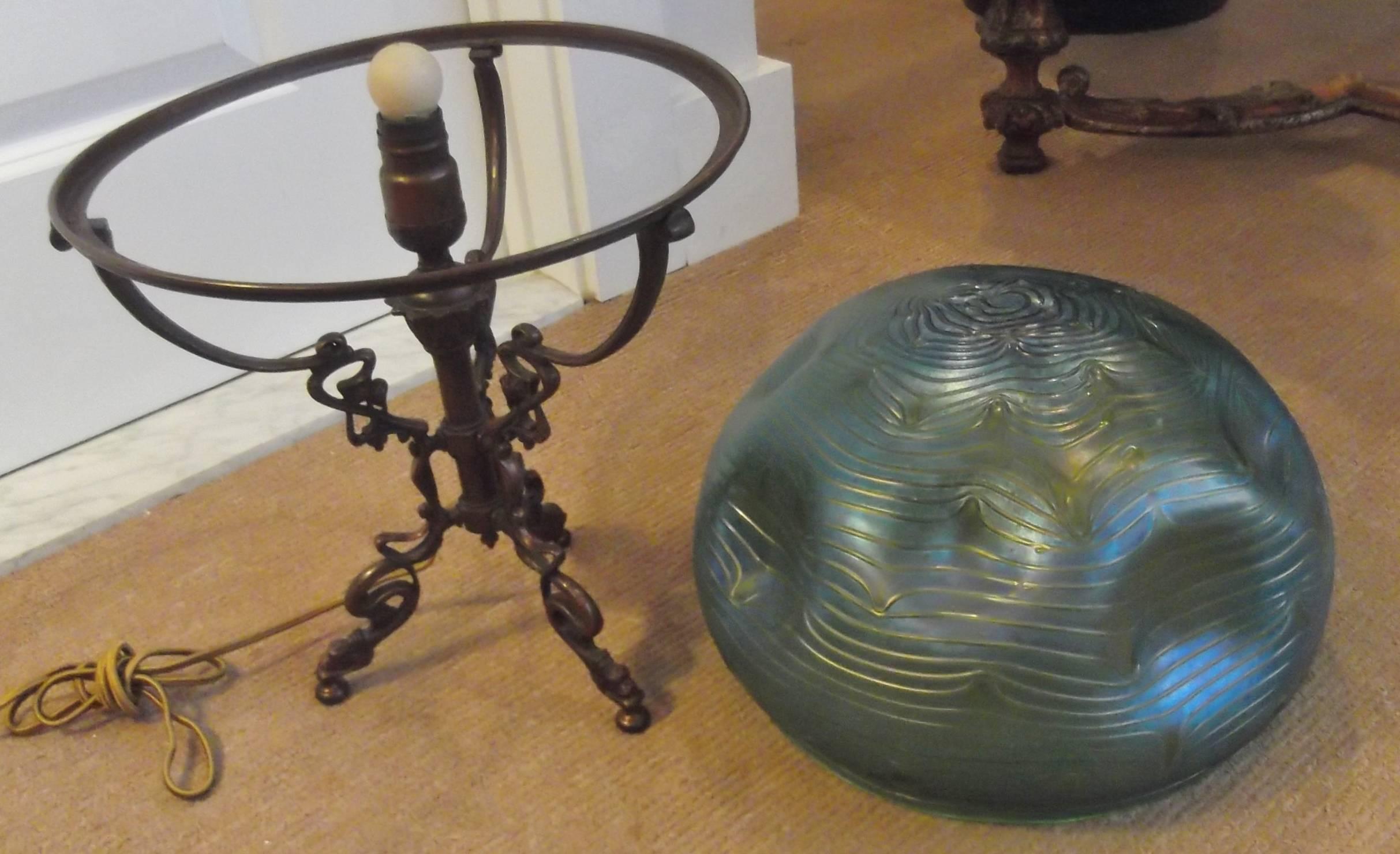 An iridescent shade with patterned and pinched glass resting on a tripod figural patinated bronze base. True Art Nouveau designed by Leopold Bauer. 12 diameter of the shade at the base.