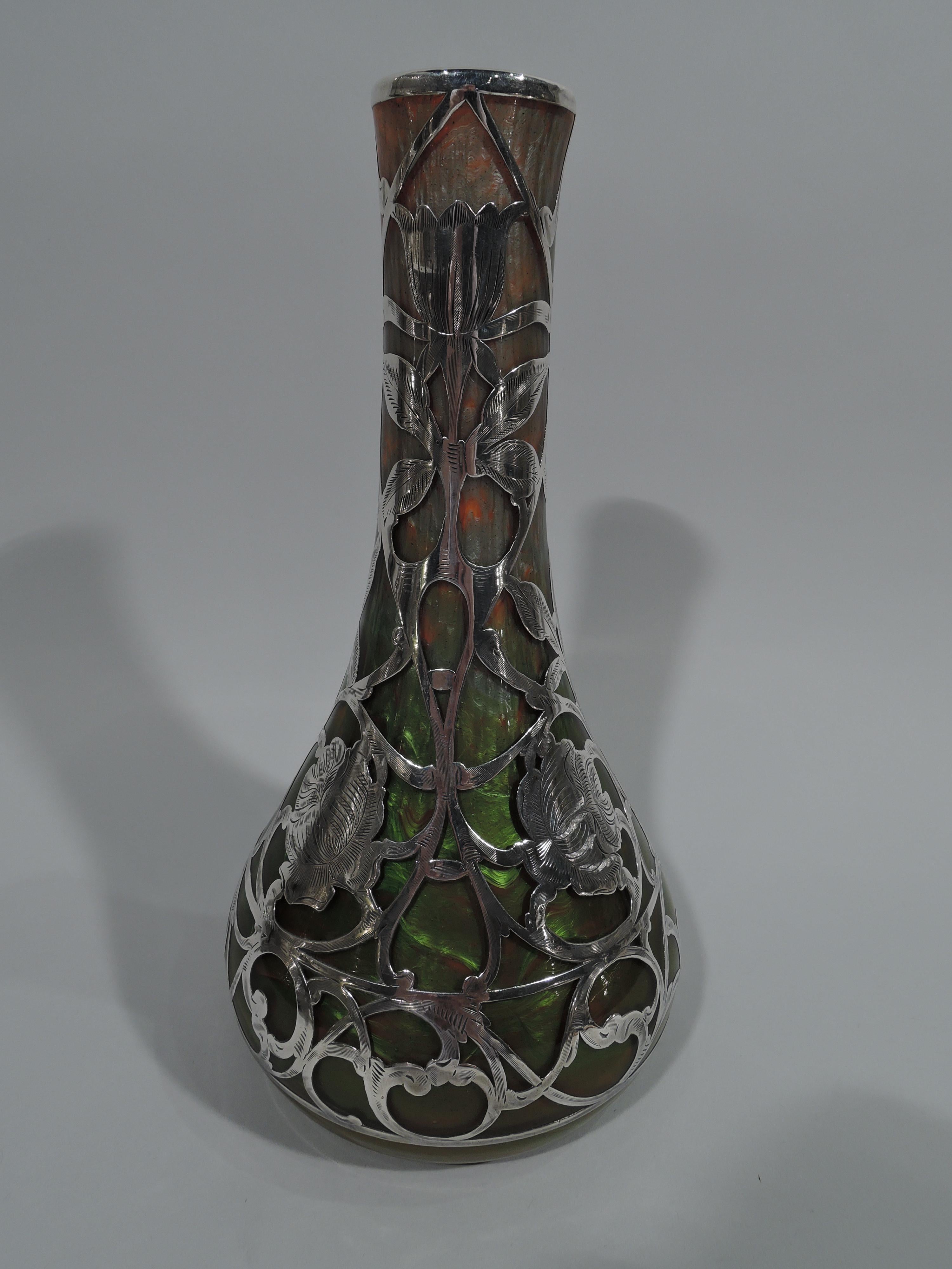 Art Nouveau iridescent glass vase in Titania pattern by historic maker Loetz, circa 1900. Conical with tall and narrow neck. Mottled and shimmering green and orange. Engraved and overlaid silver with scrolled stems and blooms. Dense and controlled.
