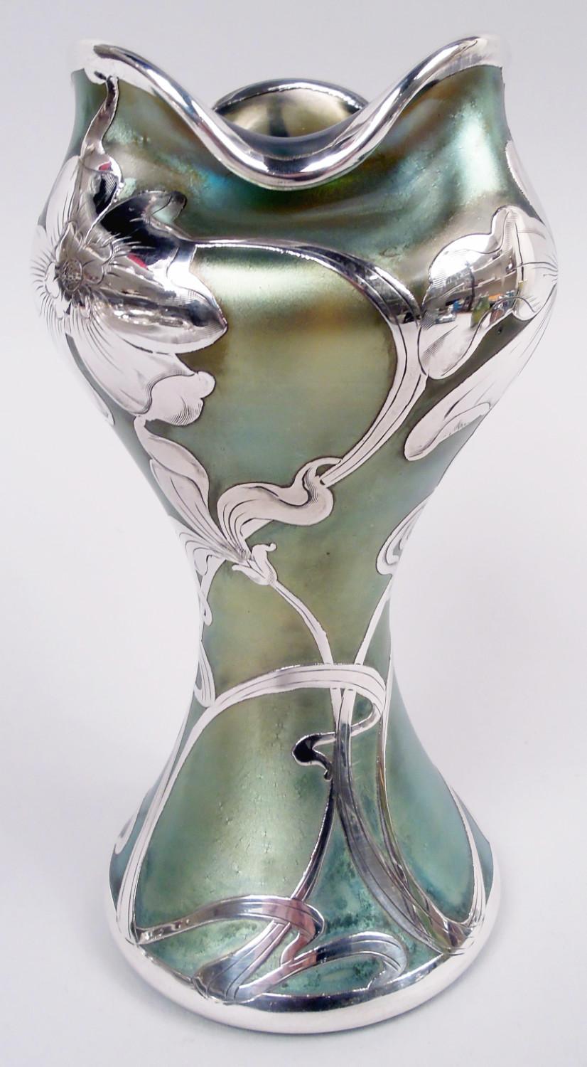 Vaso in vetro Art Nouveau dello storico Loetz con sovrapposizione di argento inciso, 1900 circa. Una forma voluttuosa, con una spalla schiacciata e una bocca ondulata e rivolta verso il basso. Sovrapposizione di viticci a frusta e capolini sciolti.
