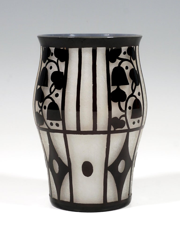 Vase on a round stand, slightly bulging towards the top with a slightly flared, flat rim of the mouth, opal-colored glass underlay with black overlay, high-cut decor with bellflowers and geometric lines on a satined background.
Design on behalf of
