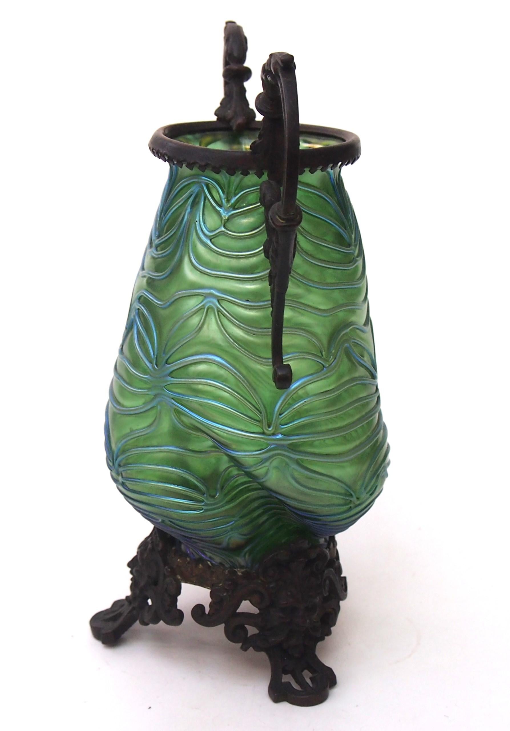 A Loetz Crete Formose wrythen gourd shaped vase in green with blue highlights an effect designed to look like waves -the vase has dramatic ornate metal handles attached to the top edge and an ornate metal base featuring three faces of Poseidon