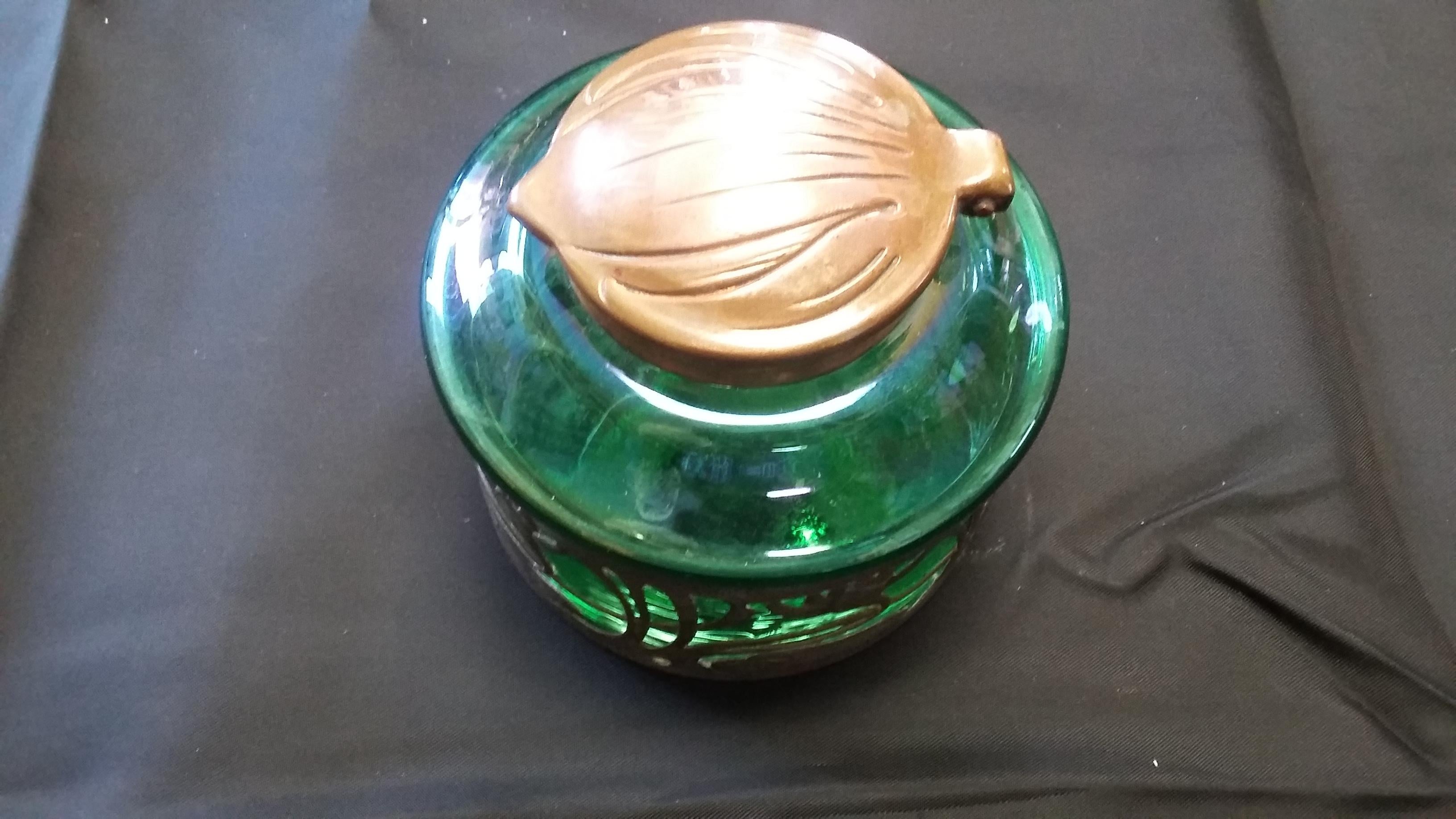 Iridescent green art glass inkwell. Has a copper top with leaf motif. The base has a plated finish with detailed flowers (Art Nouveau) style. 