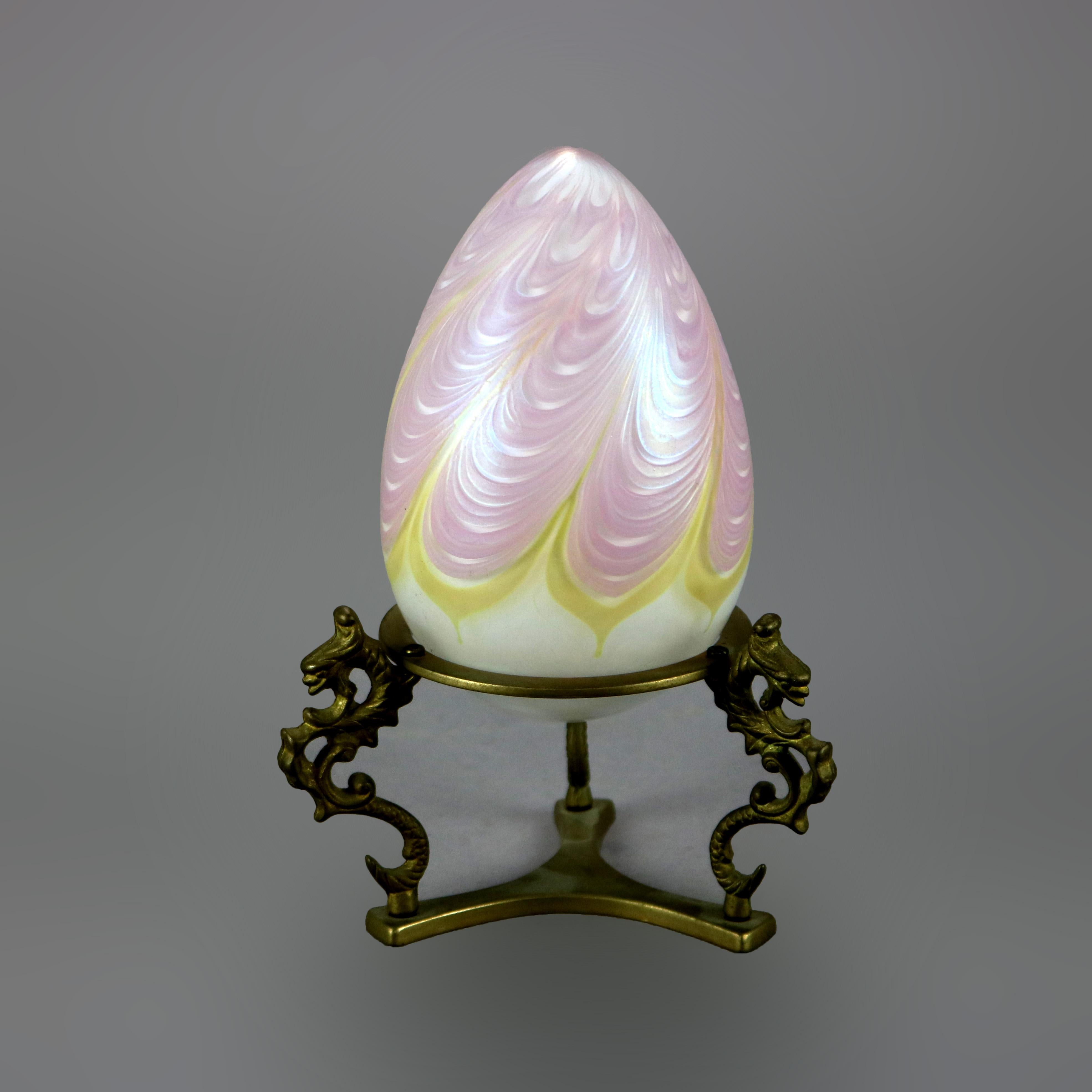 An art glass egg in the manner of Loetz offers pulled feather design and sits on figural cast brass stand having three dragon form legs, 20th century

Measures - 7.5'' H x 5'' W x 5'' D.