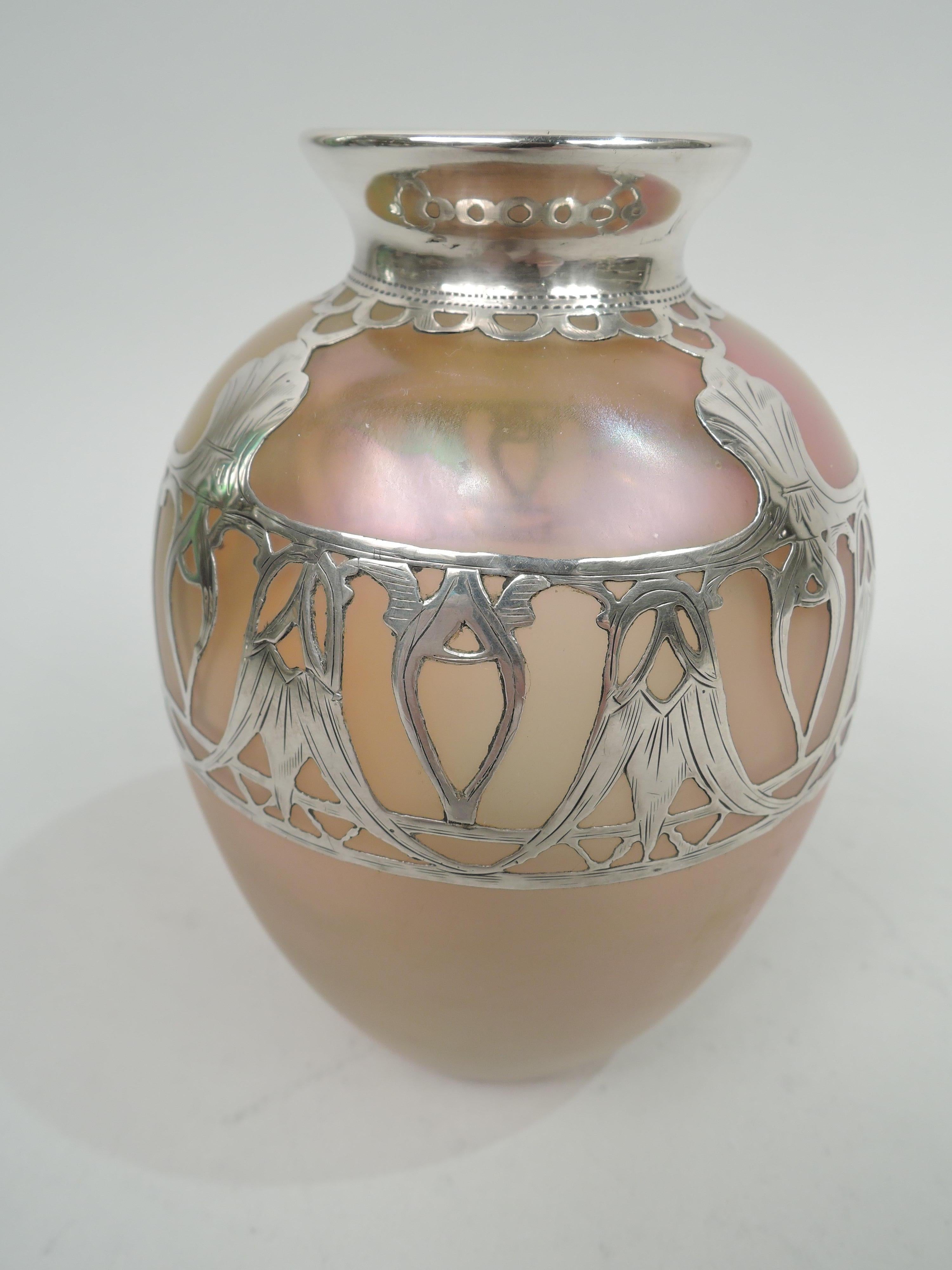 Turn-of-the-century Silberiris glass vase by Loetz with engraved silver overlay. Ovoid with flared rim in silver collar. Overlay in form of open and stylized leaf band and c-scroll neck border. Glass iridescent in orange, pink, and green.