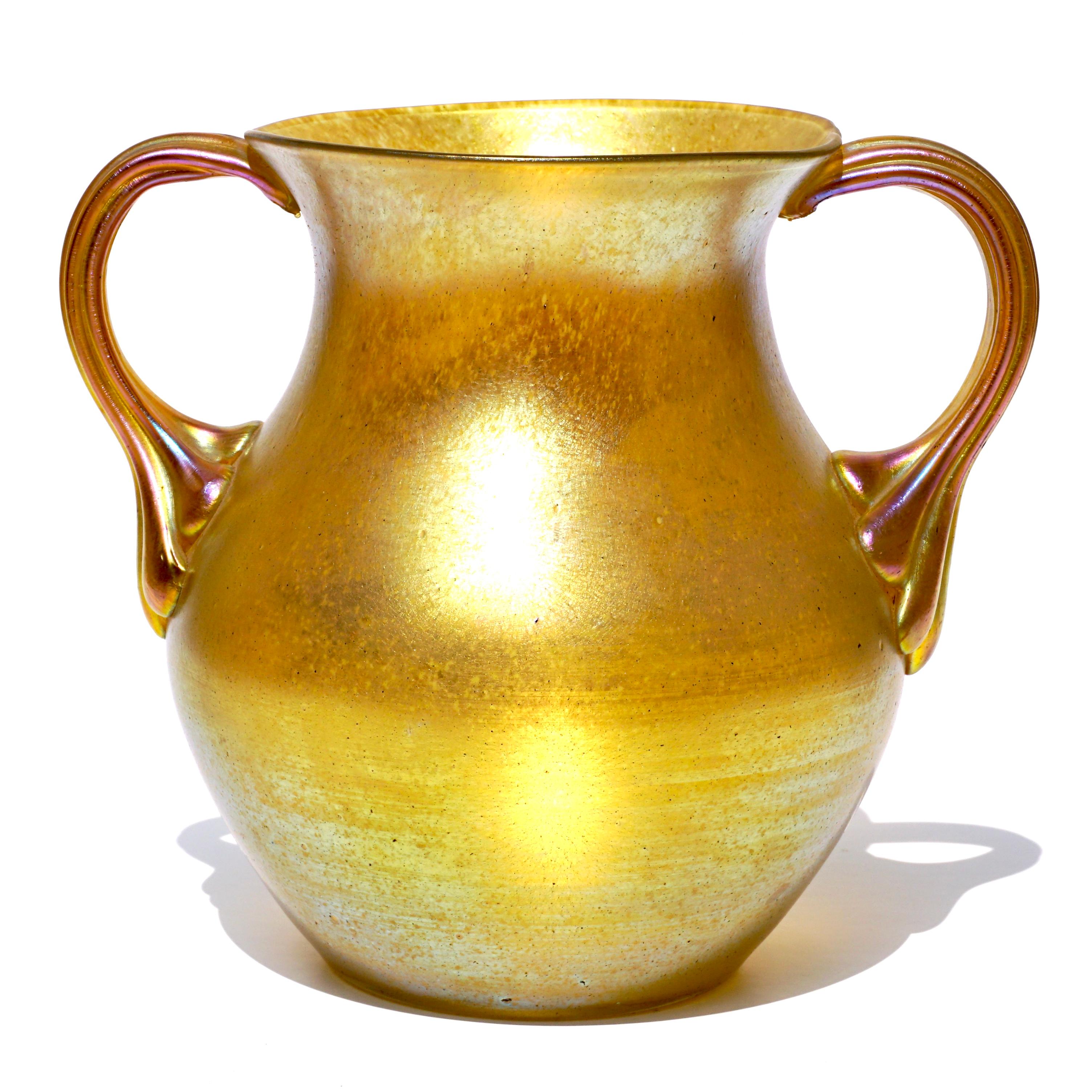 Loetz Siberiris iridescent gold glass vase with two ornate side handles, A rather large decorative vase that was the inspiration for Louis Comfort Tiffany to develope his famous Gold Favrile glass.
Height: 7.5 Inches high x 8 inch width
Condition: