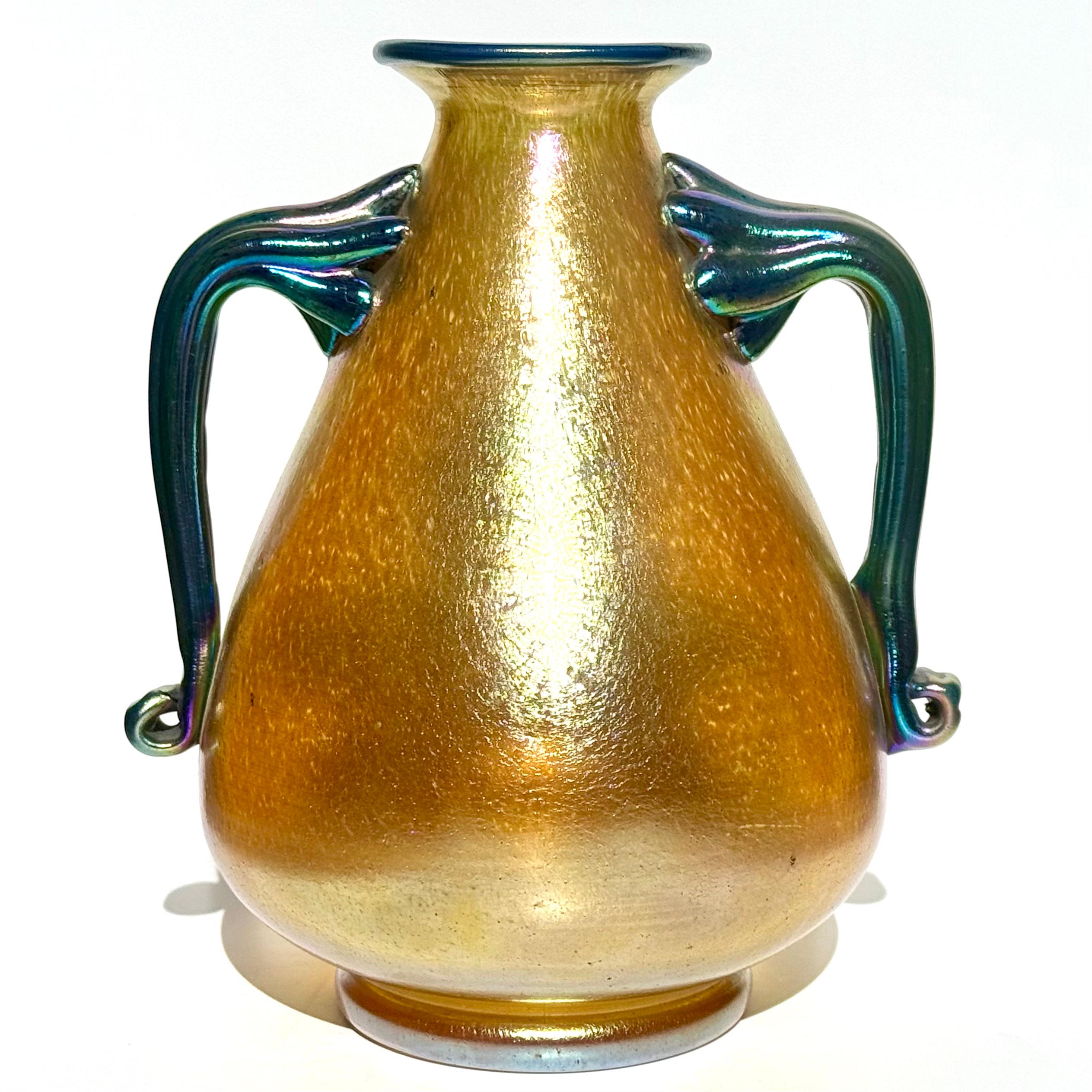 Vaso Loetz Silberiris Oro Iridescente a due manici Art Nouveau

Un delizioso vaso Loetz Silberiris con corpo conico arrotondato e due manici a nastro applicati di colore blu iridescente e bordo superiore. 
Firmato sulla base Ceco/Slovacchia. Come da
