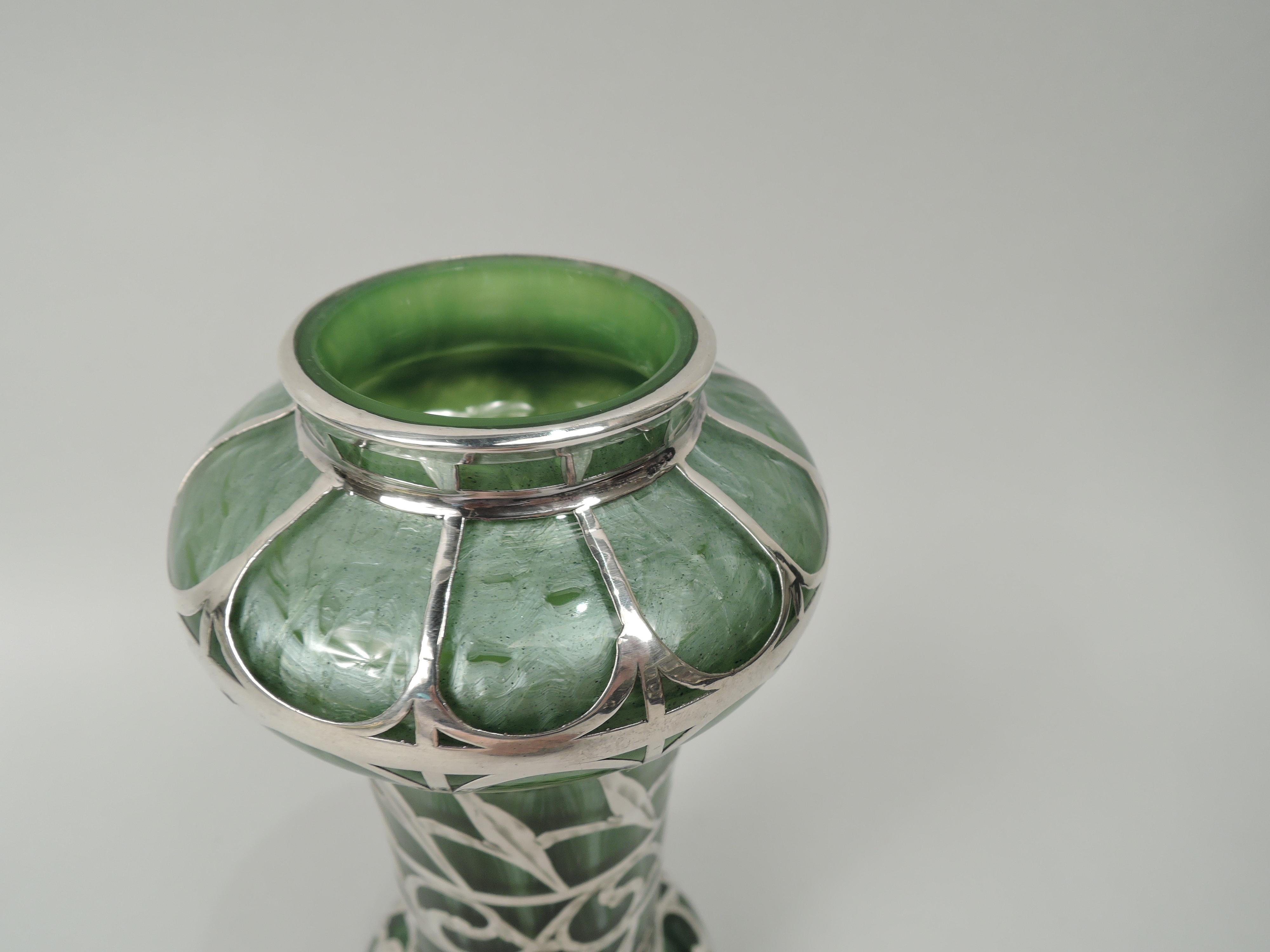 Turn-of-the-century Art Nouveau glass vase by historic maker Loetz with engraved silver overlay. Cylindrical with bellied top and bottom, and short inset neck. Overlay in form of open and horizontal pattern with stylized leaves and scrollwork. Glass