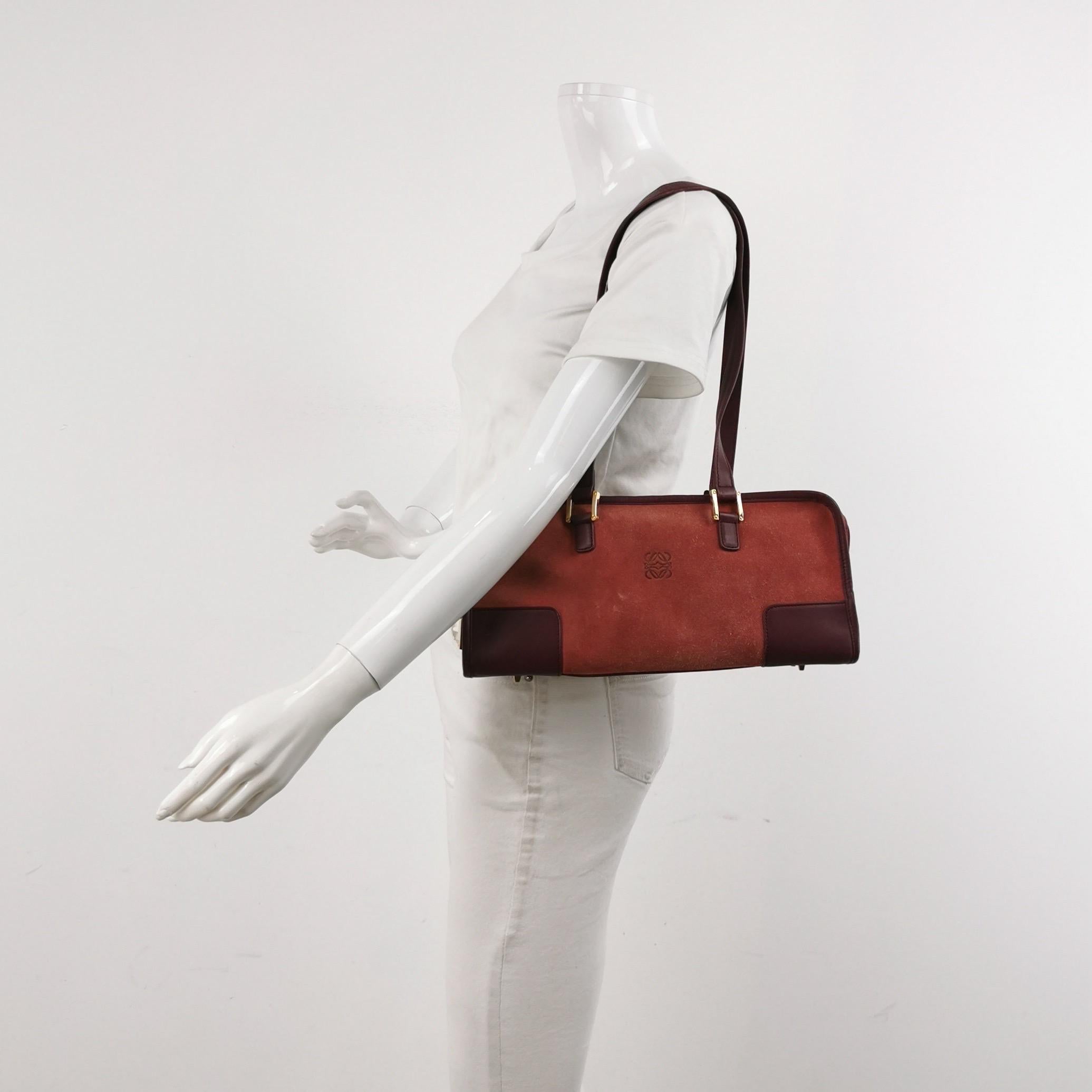 La borsa con manico in stile bauletto torna di moda nel 2024 grazie alle sfilate di Prada e Miumiu. La borsa Loewe Amazona è un'opzione elegante e funzionale per l'uso quotidiano, con una forma strutturata ma morbida. Disegnata originariamente nel