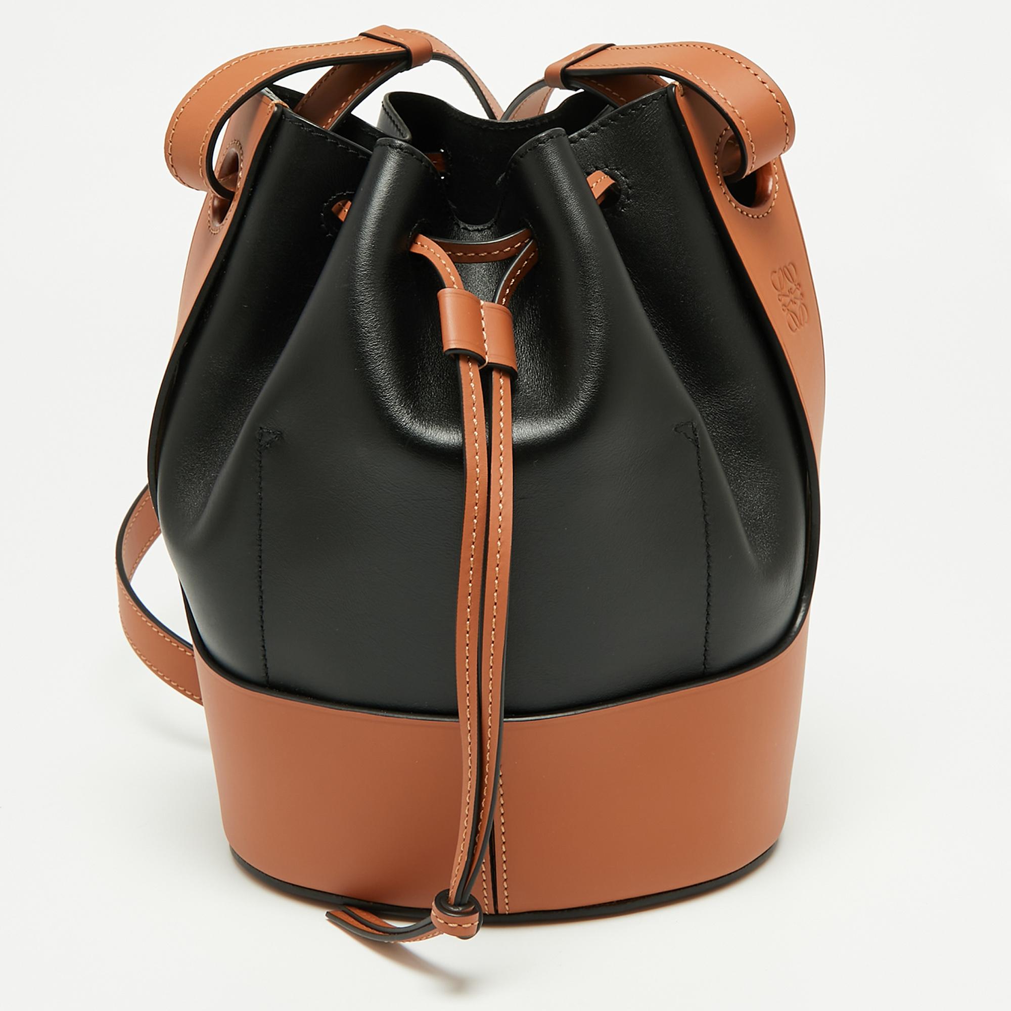 This new-age, functional Balloon bucket bag presents itself in black and tan leather, secured by a leather drawstring. It comes detailed with a long shoulder strap that can be adjusted to the desired drop. Carry your everyday essentials in the