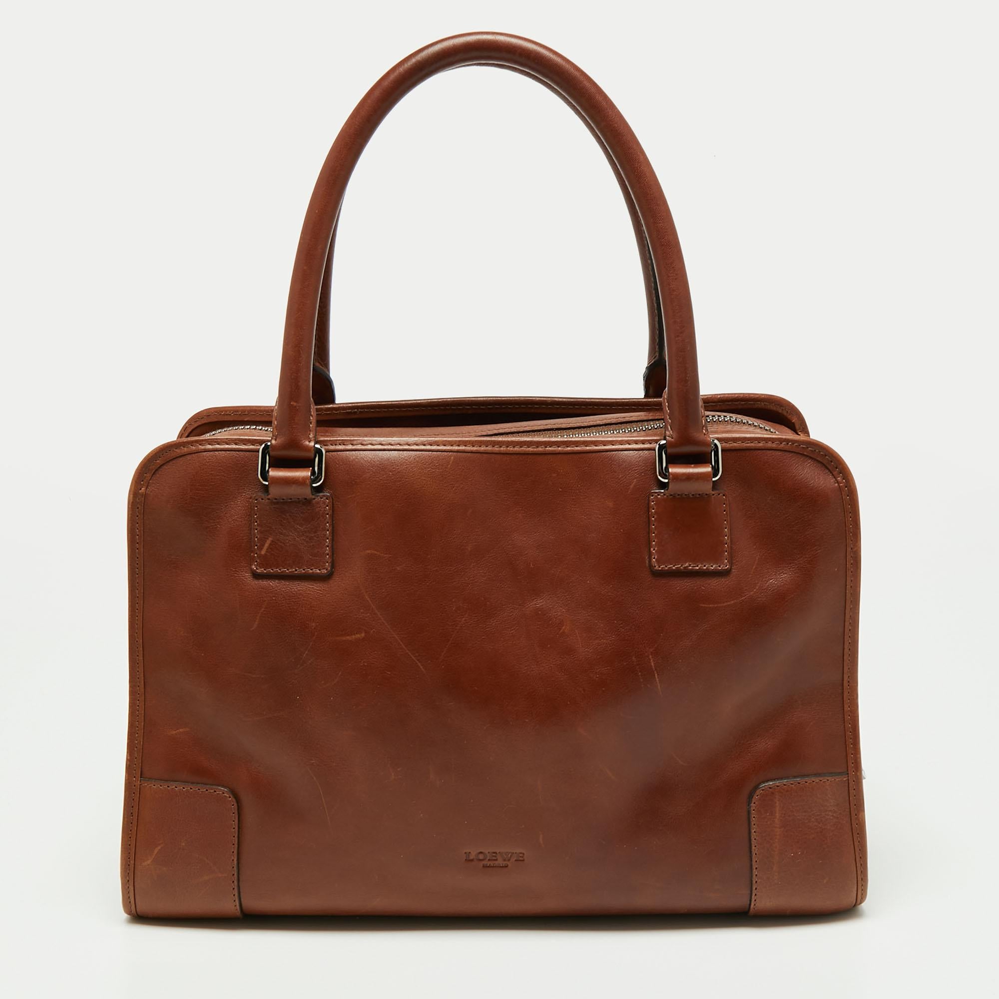 A spacious and stylish bag that can hold more than just your essentials with ease, the Amazona is one of the most popular bags from Loewe. A must-have for women on the go, it has a functional shape. Crafted in brown leather, this satchel is accented