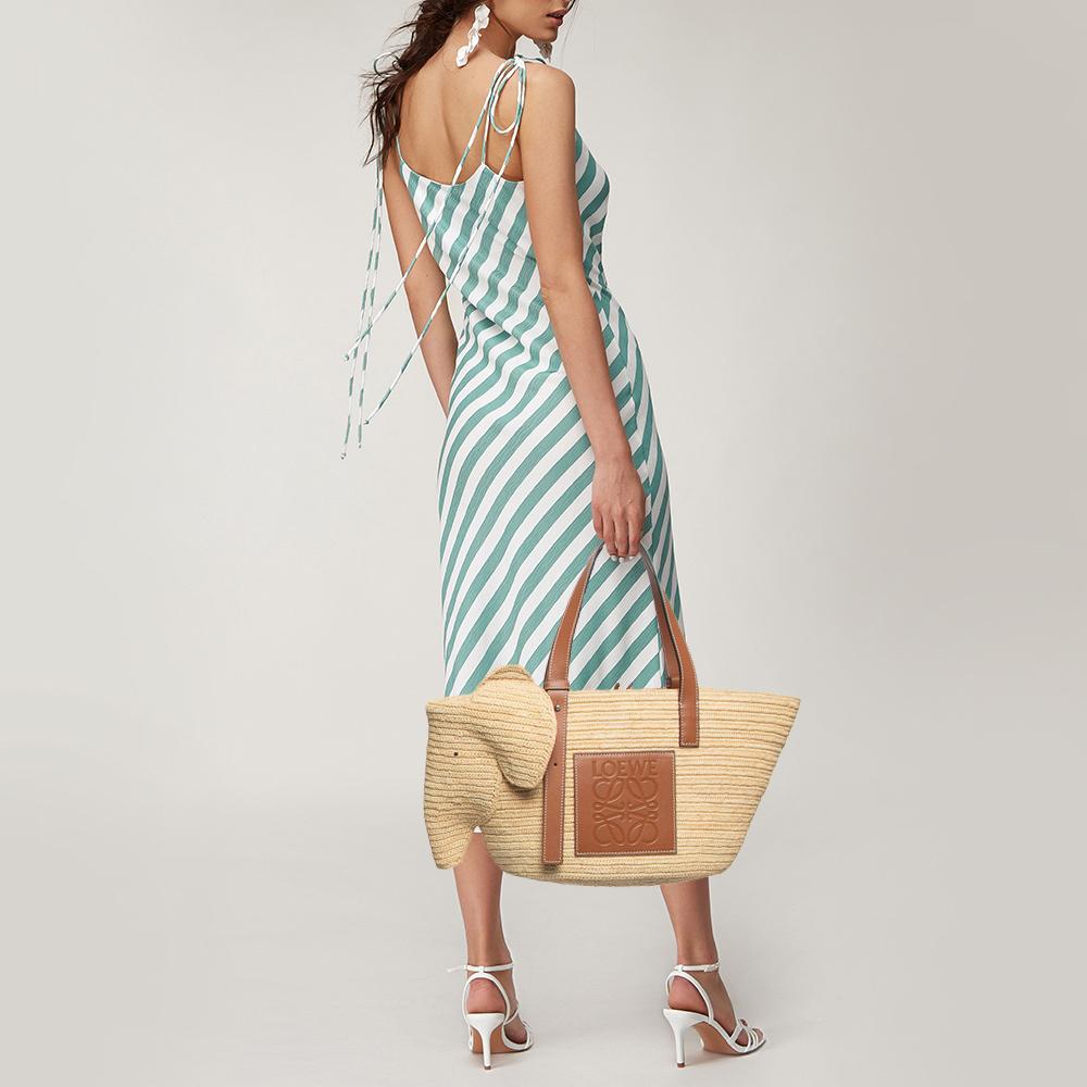 Crafted by Loewe, this exquisite basket bag epitomizes elegance and craftsmanship. The fusion of woven palm leaf and supple leather exudes sophistication. Its spacious interior and structured elephant silhouette make it both eyectahing and stylish,