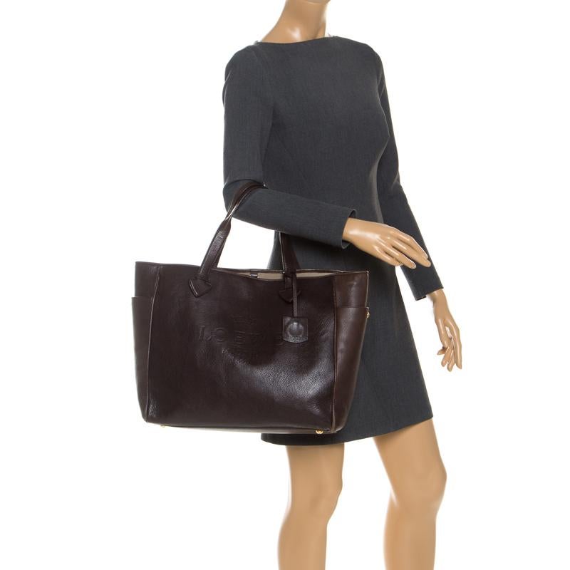 Meant for you to carry all your essentials with ease is this tote by Loewe. Crafted from leather, it comes in a stunning shade of dark brown. The bag has dual handles, two exterior side pockets, a brand logo, a nylon-lined interior with a zip pocket