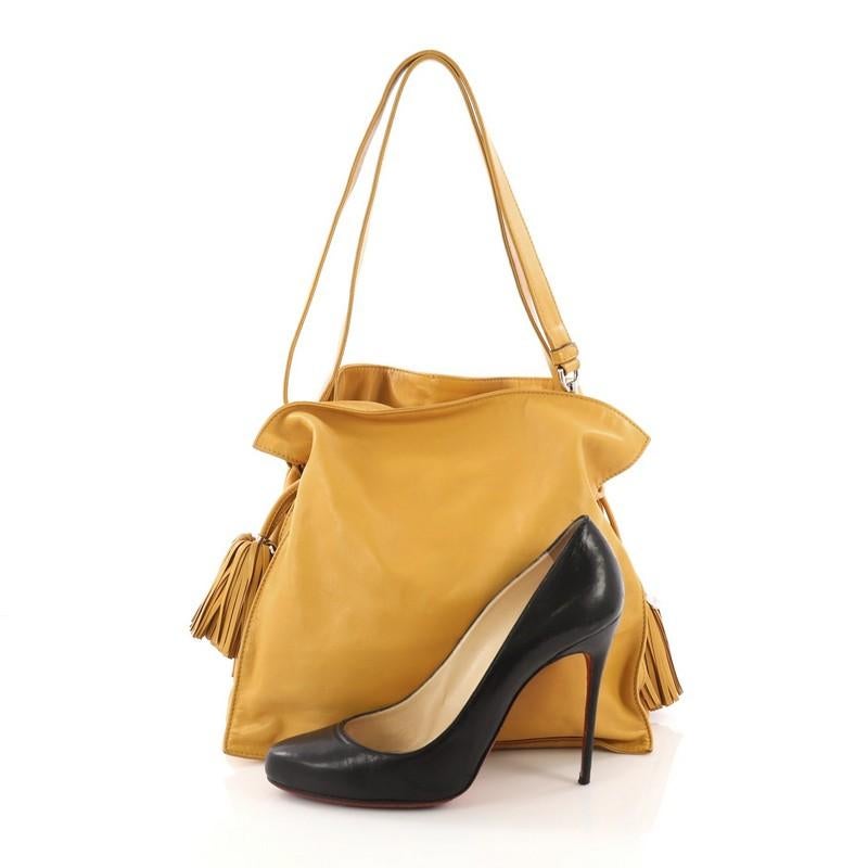 This Loewe Flamenco Bag Leather Medium, crafted in mustard yellow leather, features leather shoulder straps, drawstring top with oversized tassels, and silver-tone hardware. Its drawstring closure opens to a yellow fabric interior divided into three