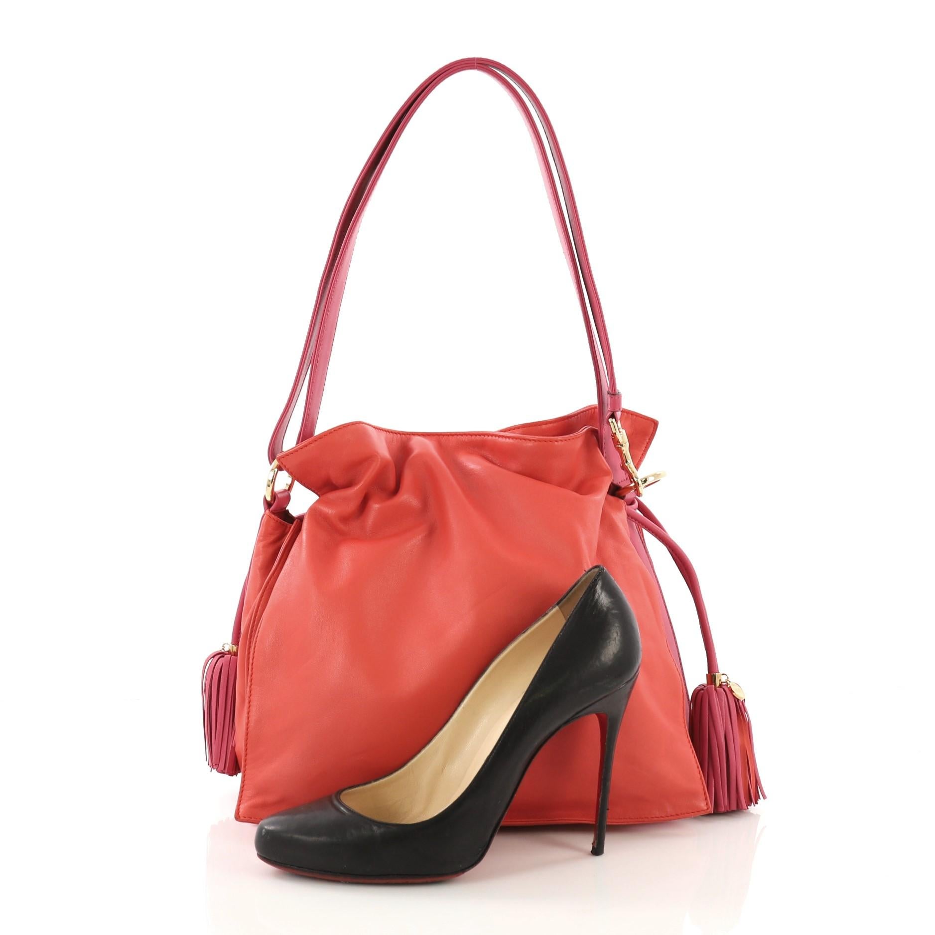 This Loewe Flamenco Bag Leather Medium, crafted in red and pink leather, features leather shoulder strap, drawstring top with tassels, and gold-tone hardware. Its drawstring closure opens to a red fabric interior divided into three compartments with