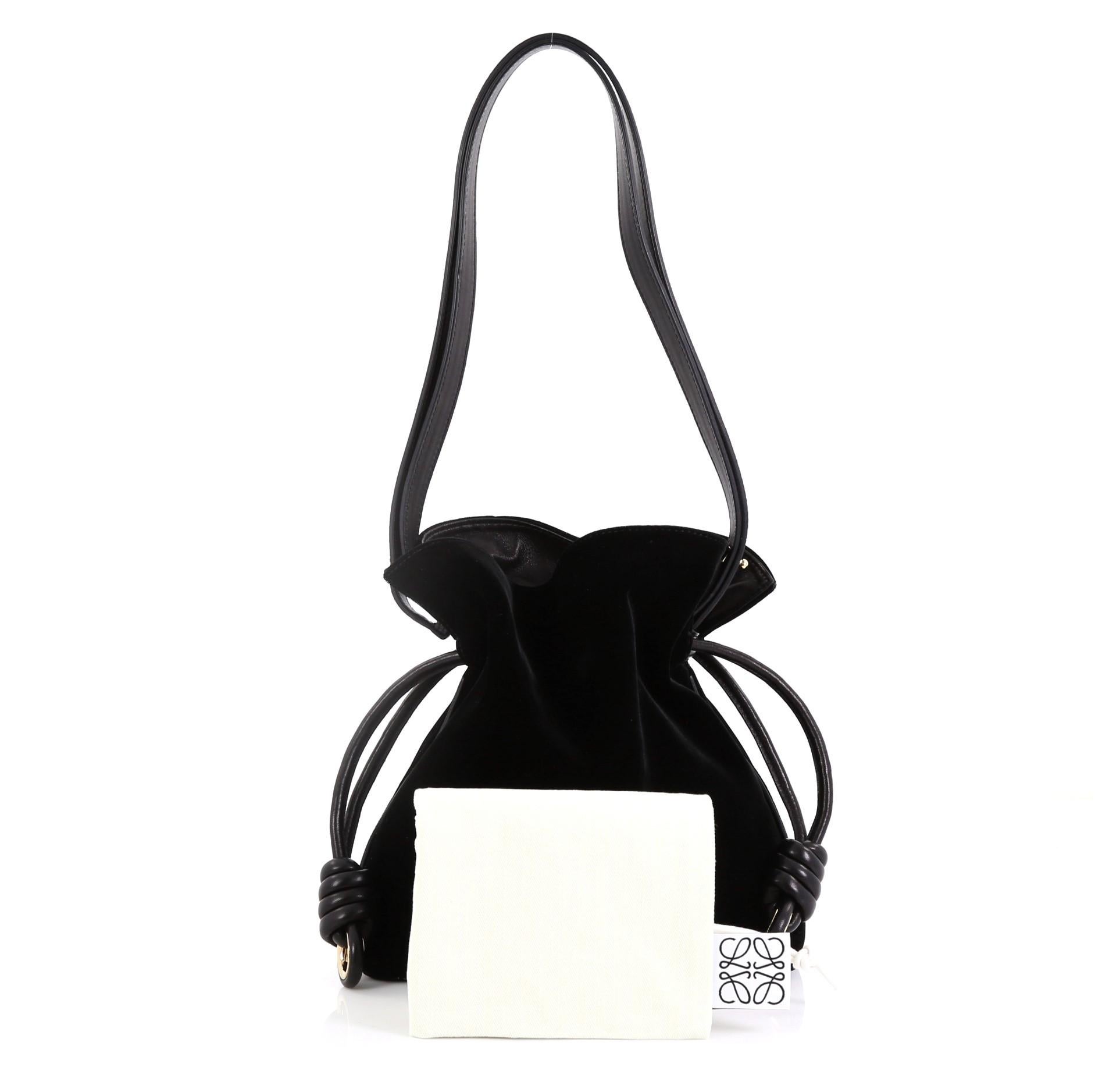 This Loewe Flamenco Knot Bag Velvet Small, crafted in black velvet and leather, features a leather shoulder strap, drawstring top with oversized knots, and gold-tone hardware. Its drawstring closure opens to a black leather interior with side snap