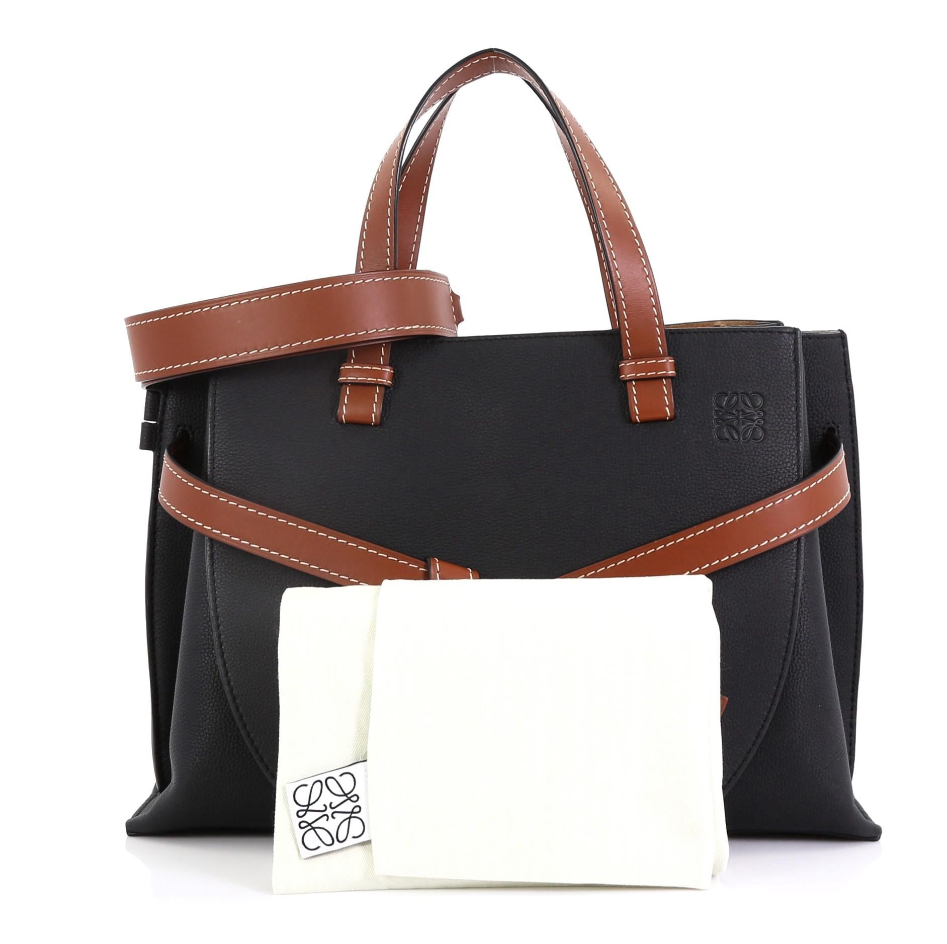 This Loewe Gate Tote Leather Small, crafted from black leather, features dual leather handles, knotted front belt bow, and gold-tone hardware. It opens to a brown suede interior with middle zip compartment and side slip pockets. 

Estimated Retail