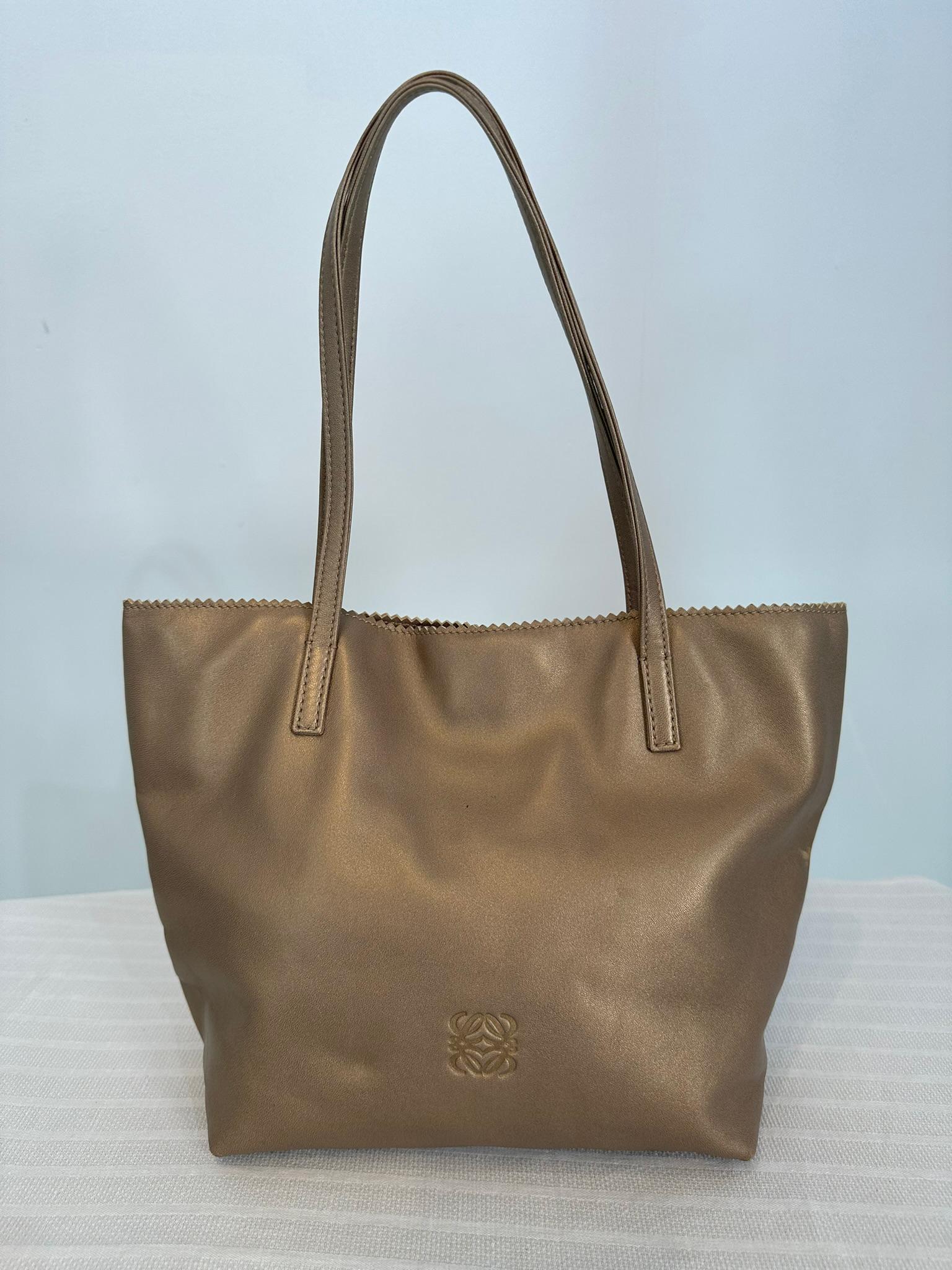 Loewe gold bronze pinked edge buttery soft leather small anagram tote double handle tote bag. Light soft Nappa leather with the anagram logo at lower front. Narrow double handle straps to carry in your hand or over your shoulder. The top edge is