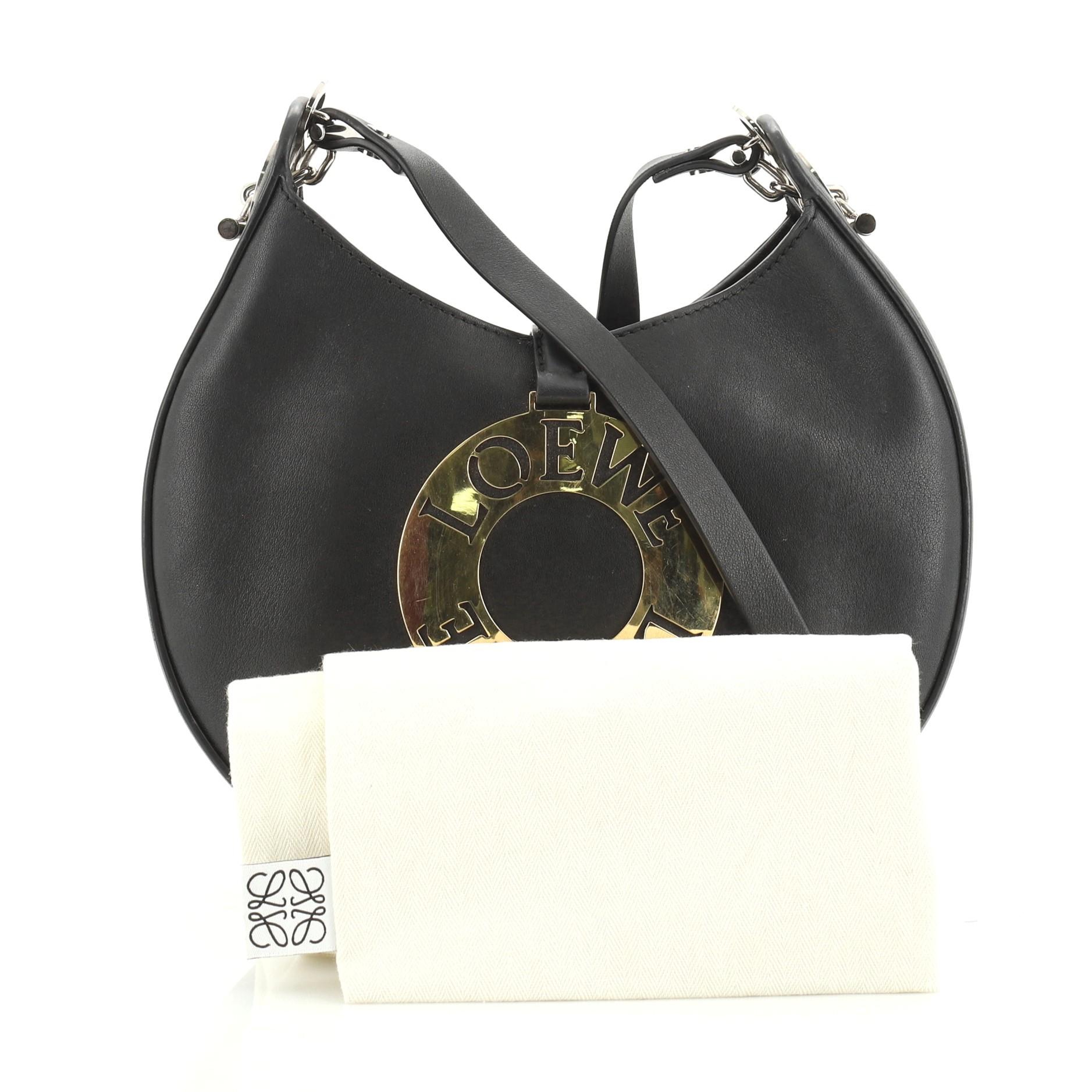This Loewe Joyce Shoulder Bag Leather Small, crafted in black leather, features a leather shoulder strap, crescent shape, jewelry-inspired gold plaque and gold and silver-tone hardware. Its snap tab closure opens to a black leather interior, with