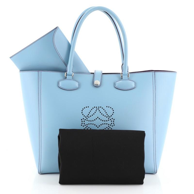 This Loewe Leo Shopper Tote Perforated Leather Medium, crafted from blue perforated leather, features dual rolled handles and silver-tone hardware. Its snap button closure opens to a purple leather interior. 

Estimated Retail Price: