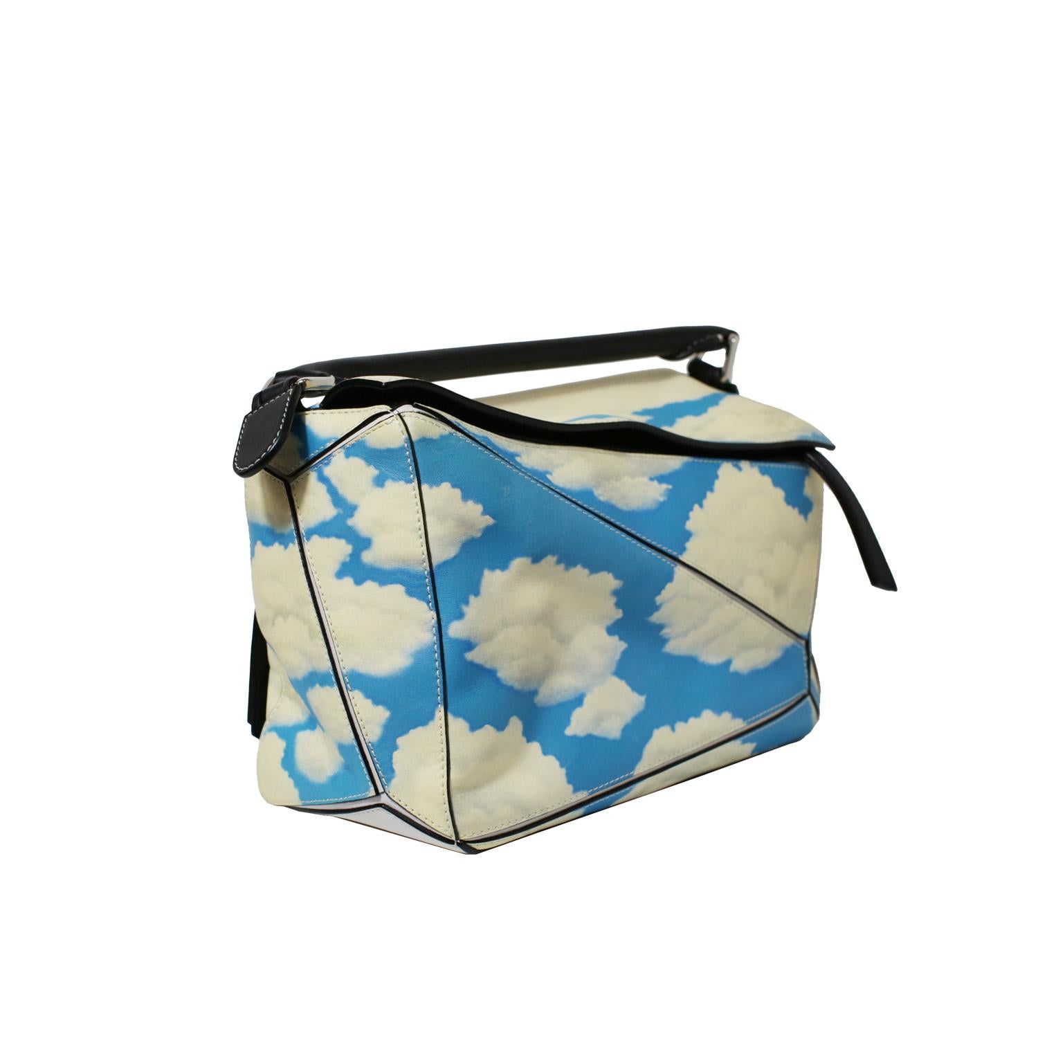 Entrez dans un rêve avec ce sac Puzzle moyen de Loewe, réimaginé dans un imprimé serein de ciel bleu et de nuages blancs. Chef-d'œuvre de design moderne et de flair artistique, ce sac présente la construction géométrique Puzzle, signature de Loewe,