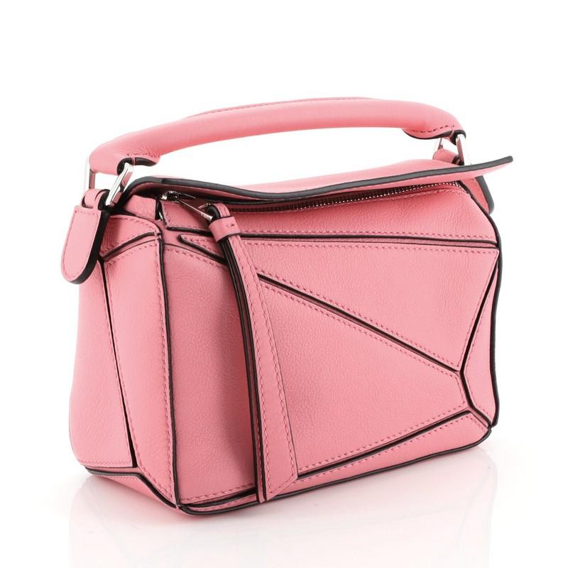 This Loewe Puzzle Bag Leather Mini, crafted in pink leather, features rolled top handle, exterior zip pocket and silver-tone hardware. Its zip closure under flap top opens to a neutral fabric interior. 

Condition: Excellent. Minor wear on base and