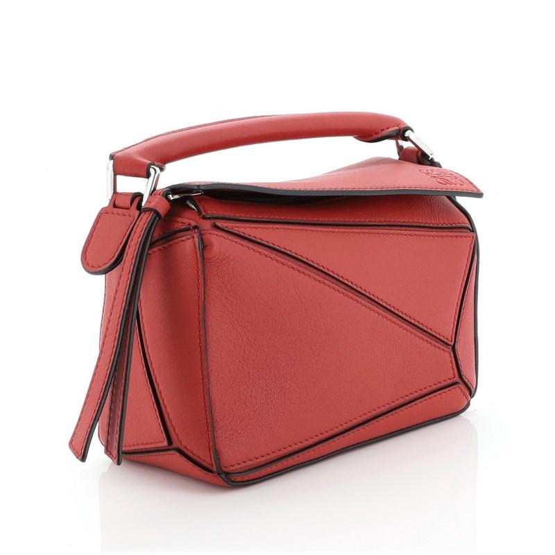 This Loewe Puzzle Bag Leather Mini, crafted in red leather, features rolled top handle, exterior zip pocket and silver-tone hardware. Its zip closure under flap top opens to a white fabric interior. 

Estimated Retail Price: $1,800
Condition: