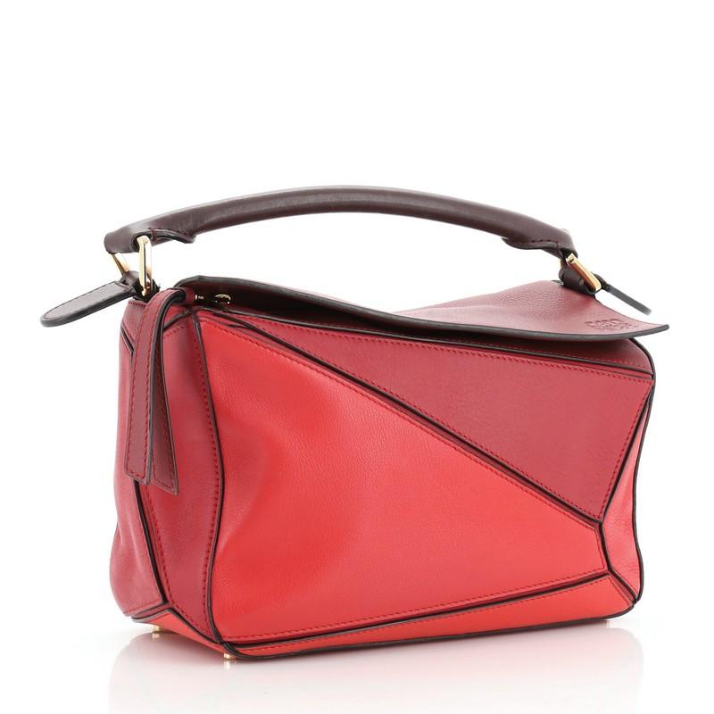 This Loewe Puzzle Bag Leather Small, crafted in red leather, features rolled top handle, exterior zip pocket and gold-tone hardware. Its zip closure under flap top opens to a black fabric interior. 

Estimated Retail Price: $1,990
Condition: Good.