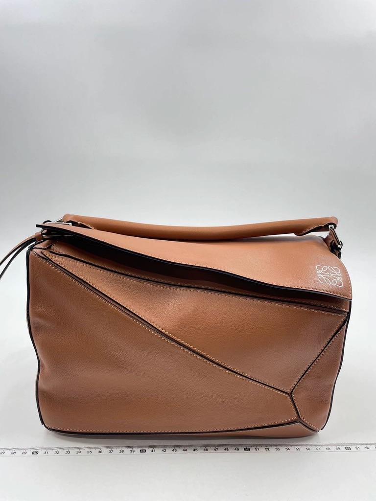 Loewe's Puzzle bag is a timeless classic cult piece. Crafted from supple caramel leather and finished with silver hardware and signature origami-inspired panels, this bag is versatile and stylish. It can be used as a tote or folded to fit under your